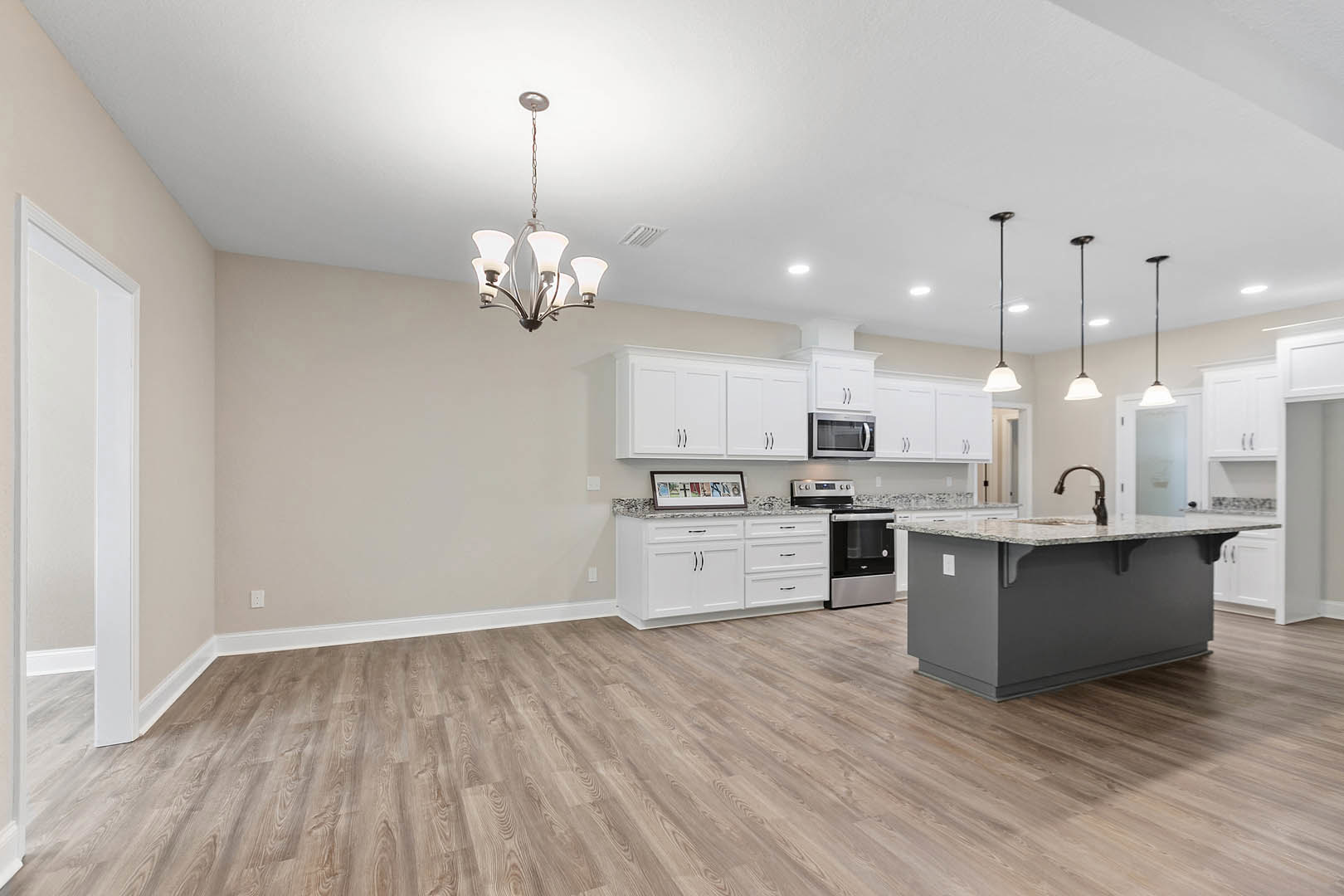 Kitchen with hardwood flooring, white shaker cabinets, marble-topped island, stainless steel stove and microwave, framed wall art with letters