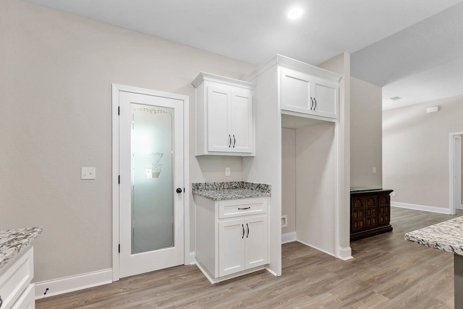 White kitchen cabinets with black handles, marble countertop, glass door leading outside, white light switch on wall, stainless steel sink and appliances