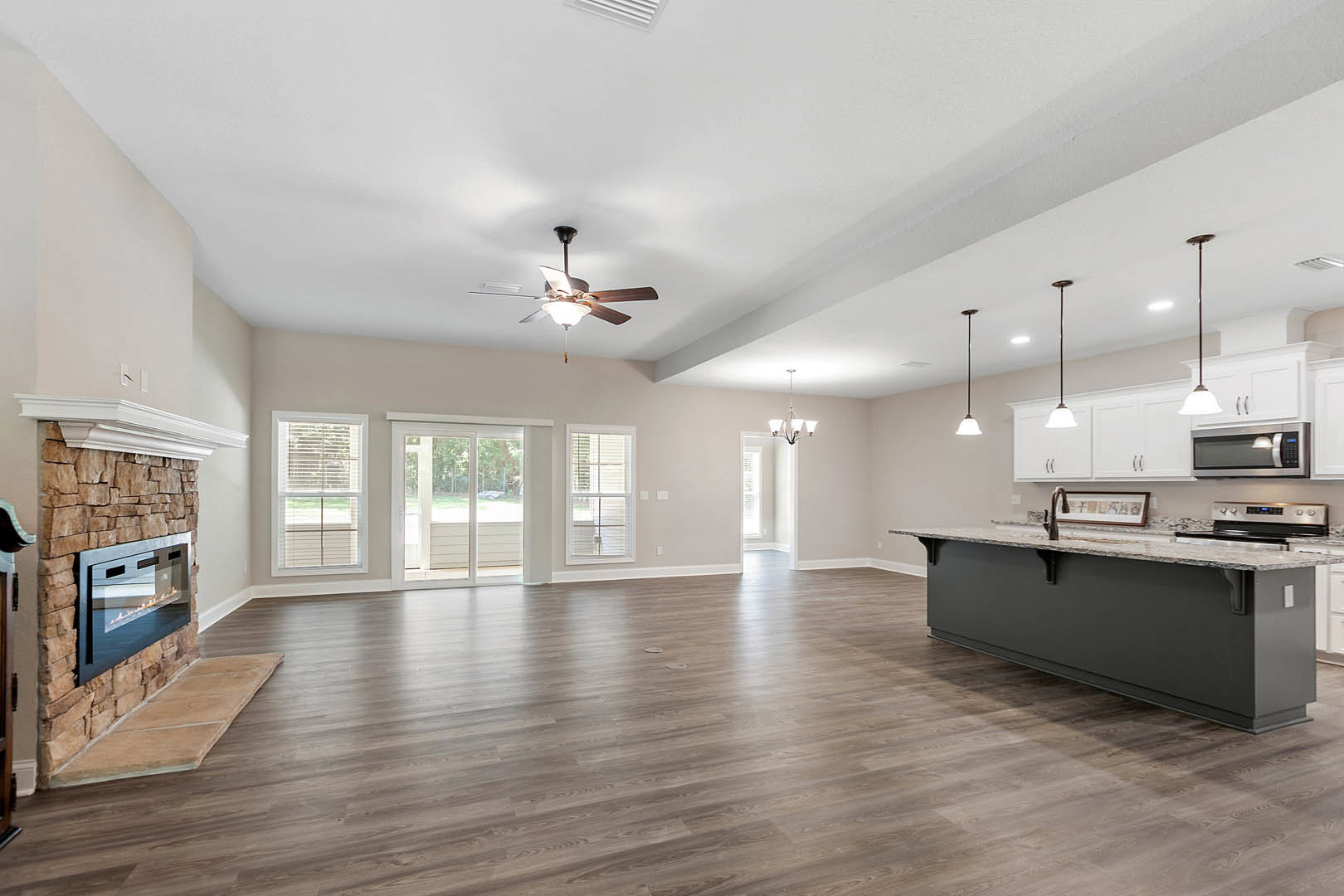 Open floor plan featuring hardwood flooring, spacious kitchen with central island, white cabinetry, stone countertops, ceiling fan with light fixture, and modern fireplace