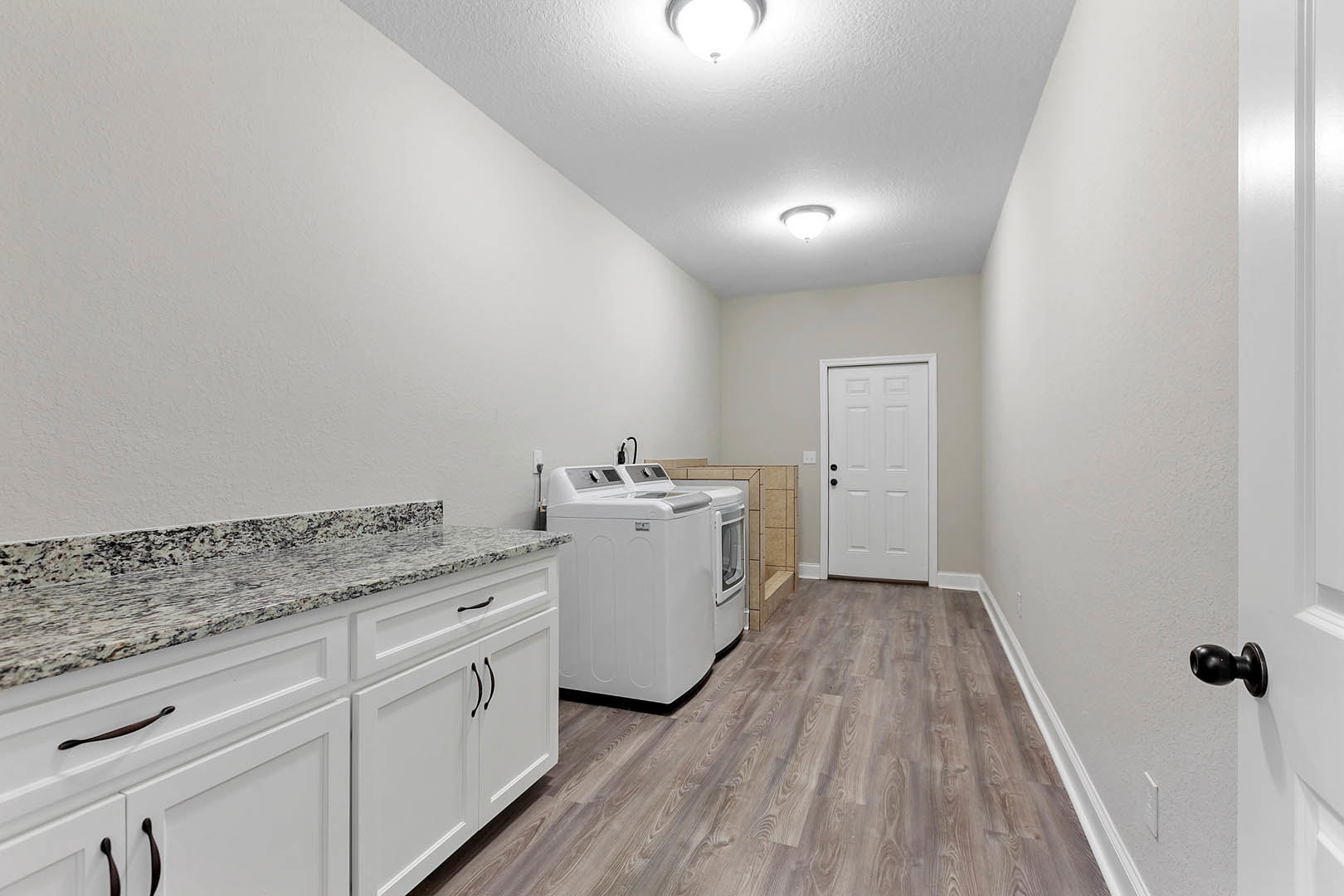 Laundry room featuring white shaker cabinets, marble countertops, white front-loading washing machine, black hardware, and overhead ceiling light