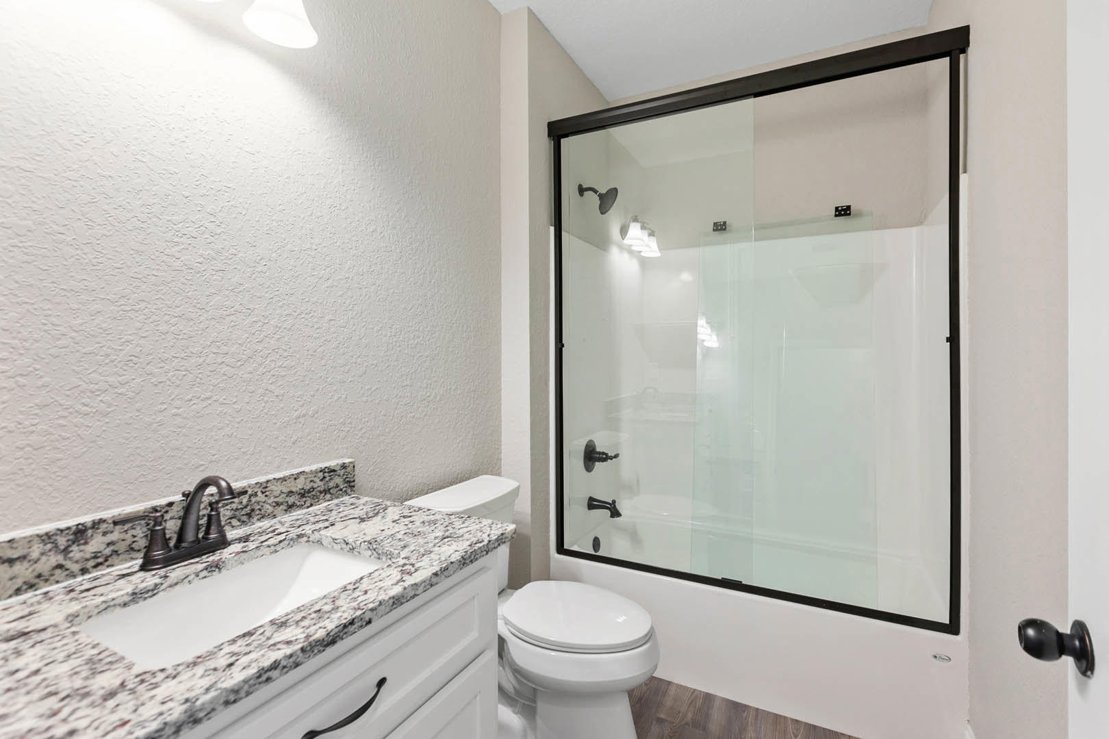 Bathroom with glass shower door, white tile walls, black faucet on rectangular sink, closed white toilet, chrome shower fixtures