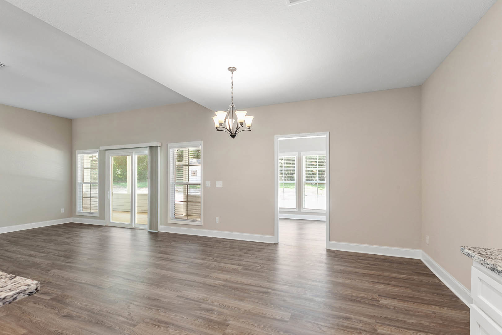 Hardwood floor room with white plaster ceiling, ornate chandelier, and window fitted with white blinds