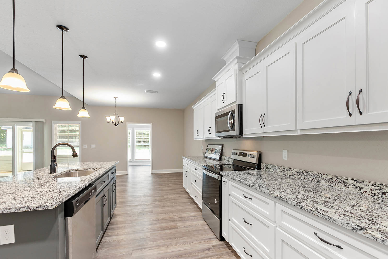 White kitchen cabinets with brushed metal hardware, granite countertops, stainless steel microwave, framed picture on counter, white electrical outlet, and chrome support pole near