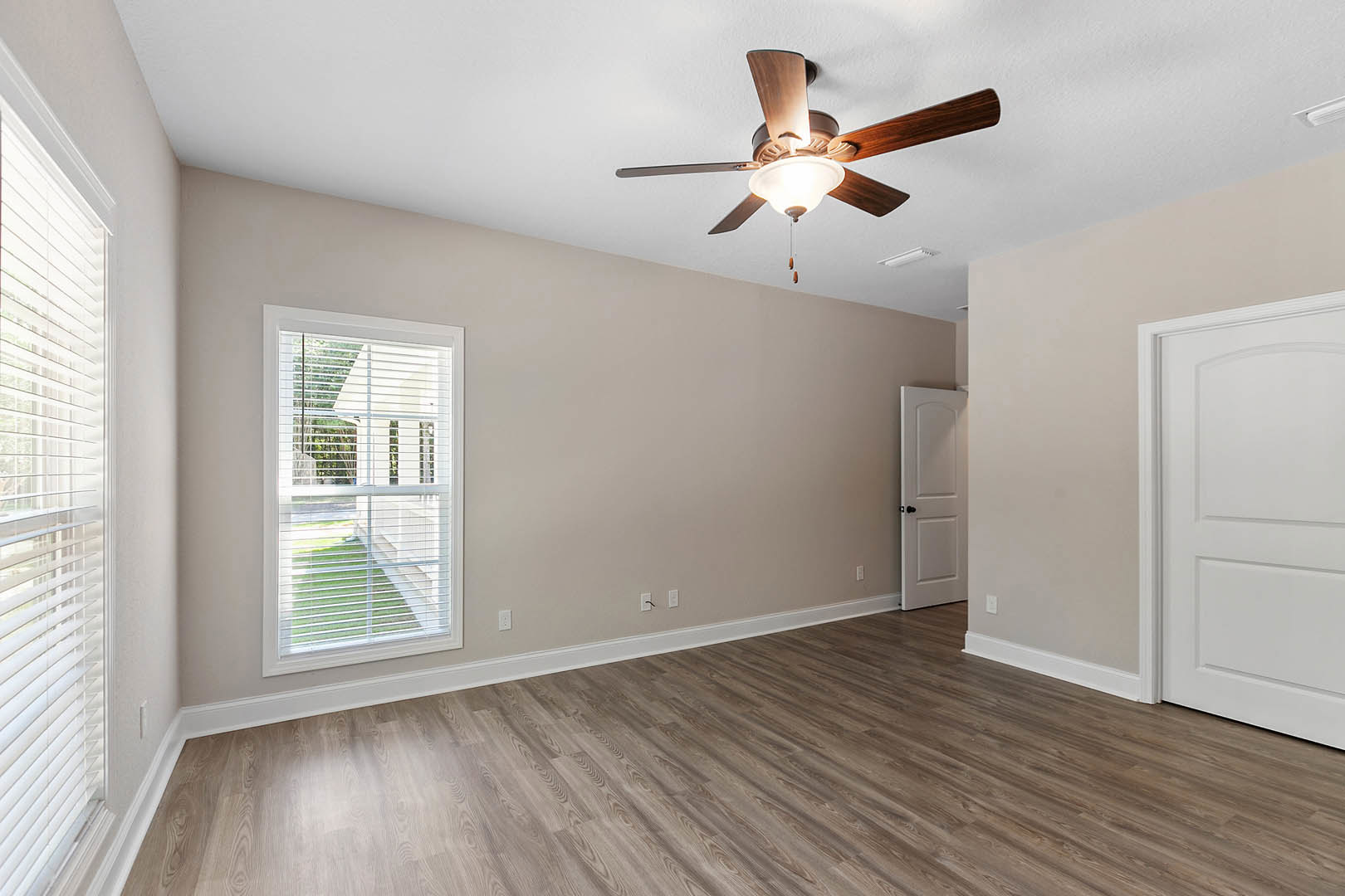 Ceiling fan with light fixture above wood flooring, white baseboards, window with blinds, and white door with black knobs