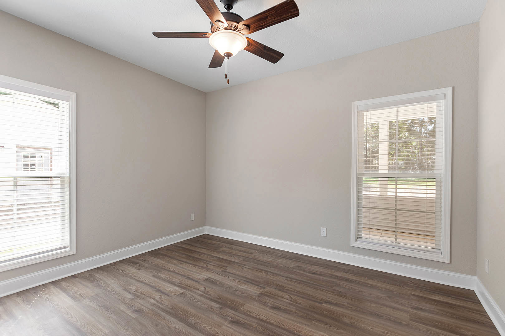 Ceiling fan with light fixture mounted above wood flooring, white baseboards, and a window with closed blinds in a neutral-toned room