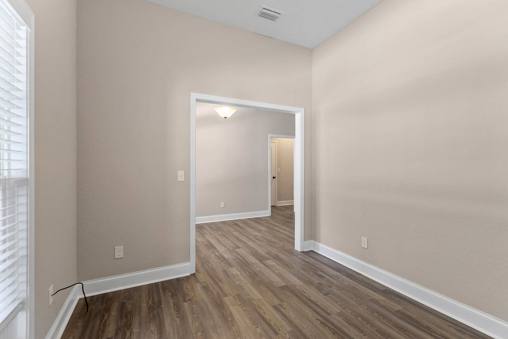 Hallway with light wood flooring, white baseboards, white door with black knobs, white door frame, and ceiling light fixture