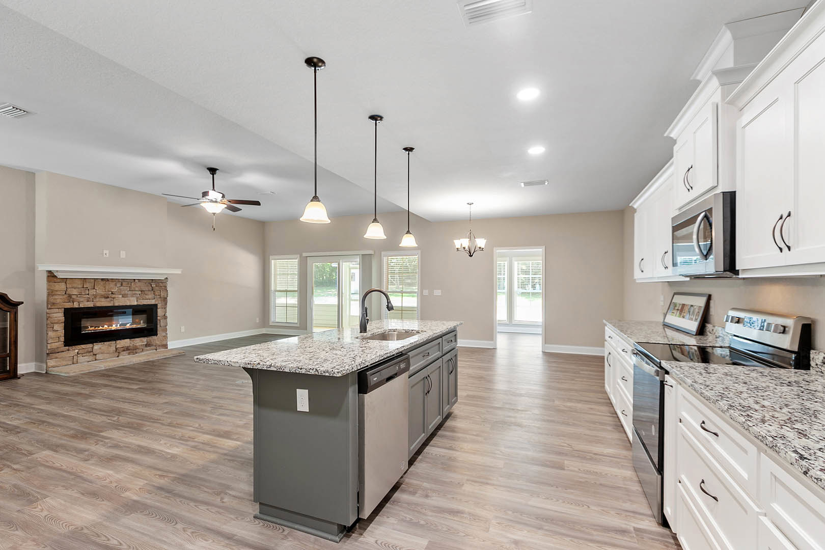 Spacious kitchen featuring a stone fireplace with active fire, expansive island with built-in sink and dishwasher, white cabinetry, wood flooring, and recessed lighting.