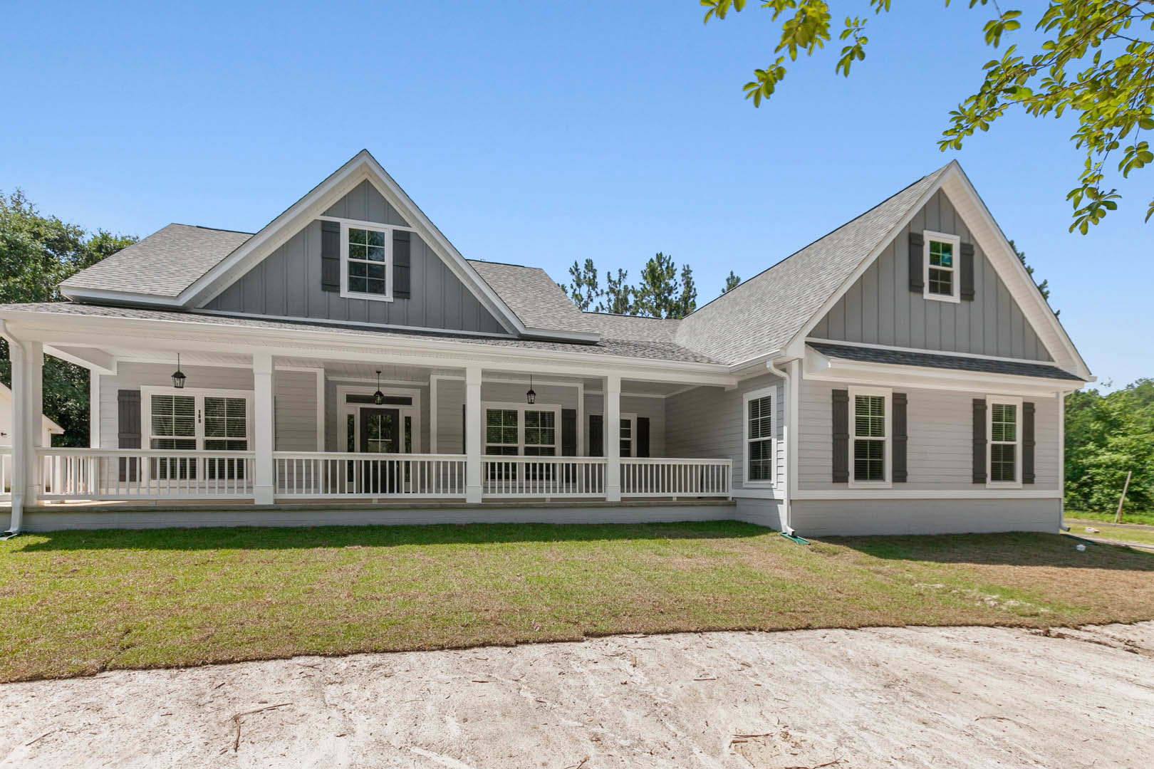 White clapboard house with covered porch, grid windows, and shutters, bordered by a lawn and gravel driveway; mature trees and Robert Frost Farm visible in the background.