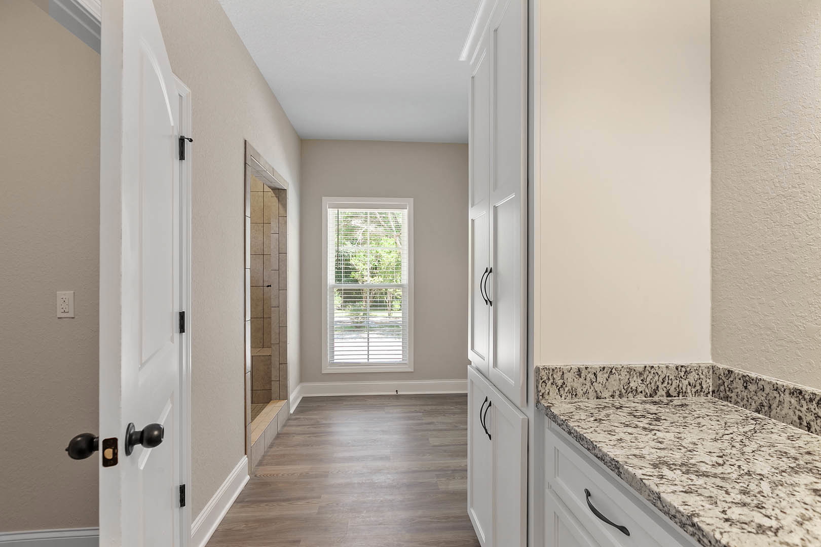 Hallway featuring white cabinets with black handles, marble countertop with black and white speckles, wood and tile flooring, window with blinds, and plumbing fixture.