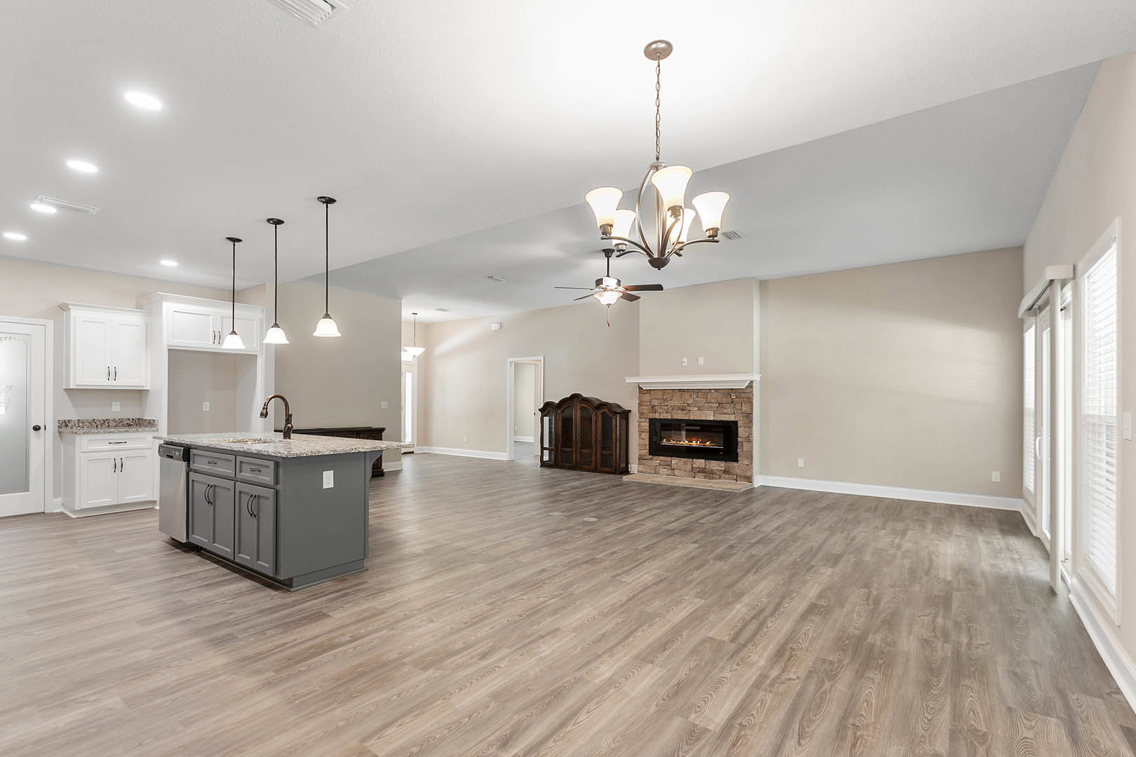 Spacious open floor plan featuring a kitchen island with granite countertops, wooden cabinets with glass doors, hardwood flooring, and a stone wall fireplace