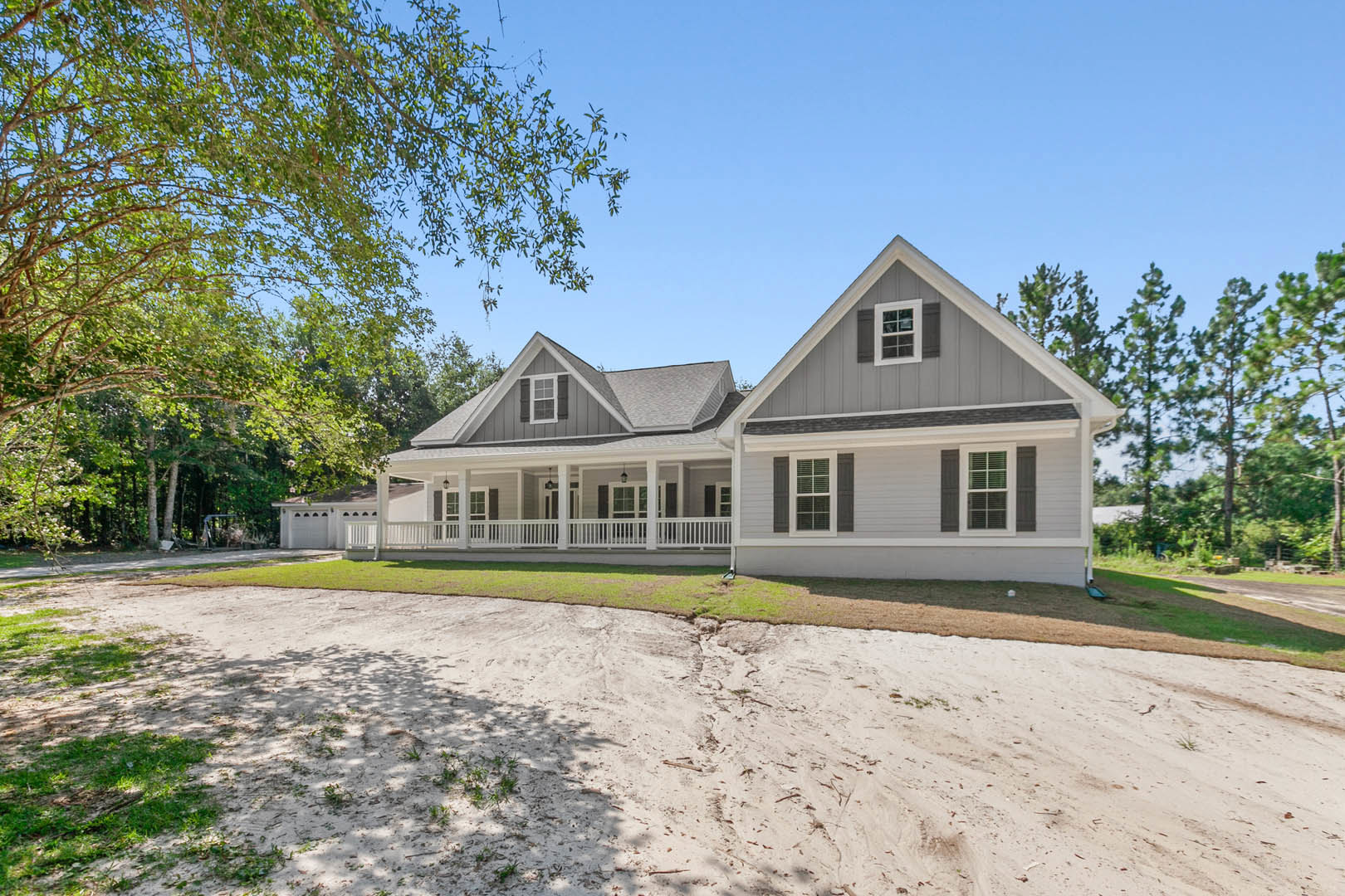 White-painted porch with multiple columns, wide steps, and a tree in front; large windows with white frames and blinds; light-colored siding and landscaped yard.
