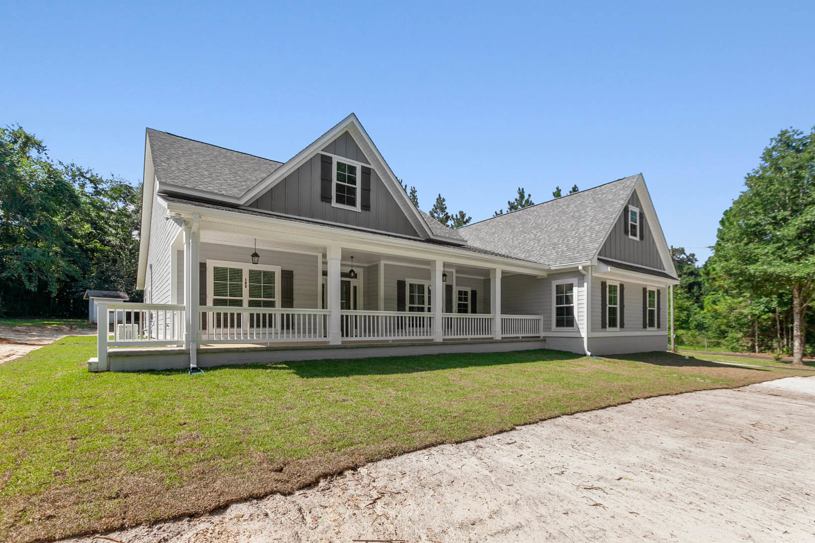 White clapboard house with covered porch, multi-pane windows, and paved driveway bordered by green lawn; mature trees and historic Robert Frost Farm visible in the background.