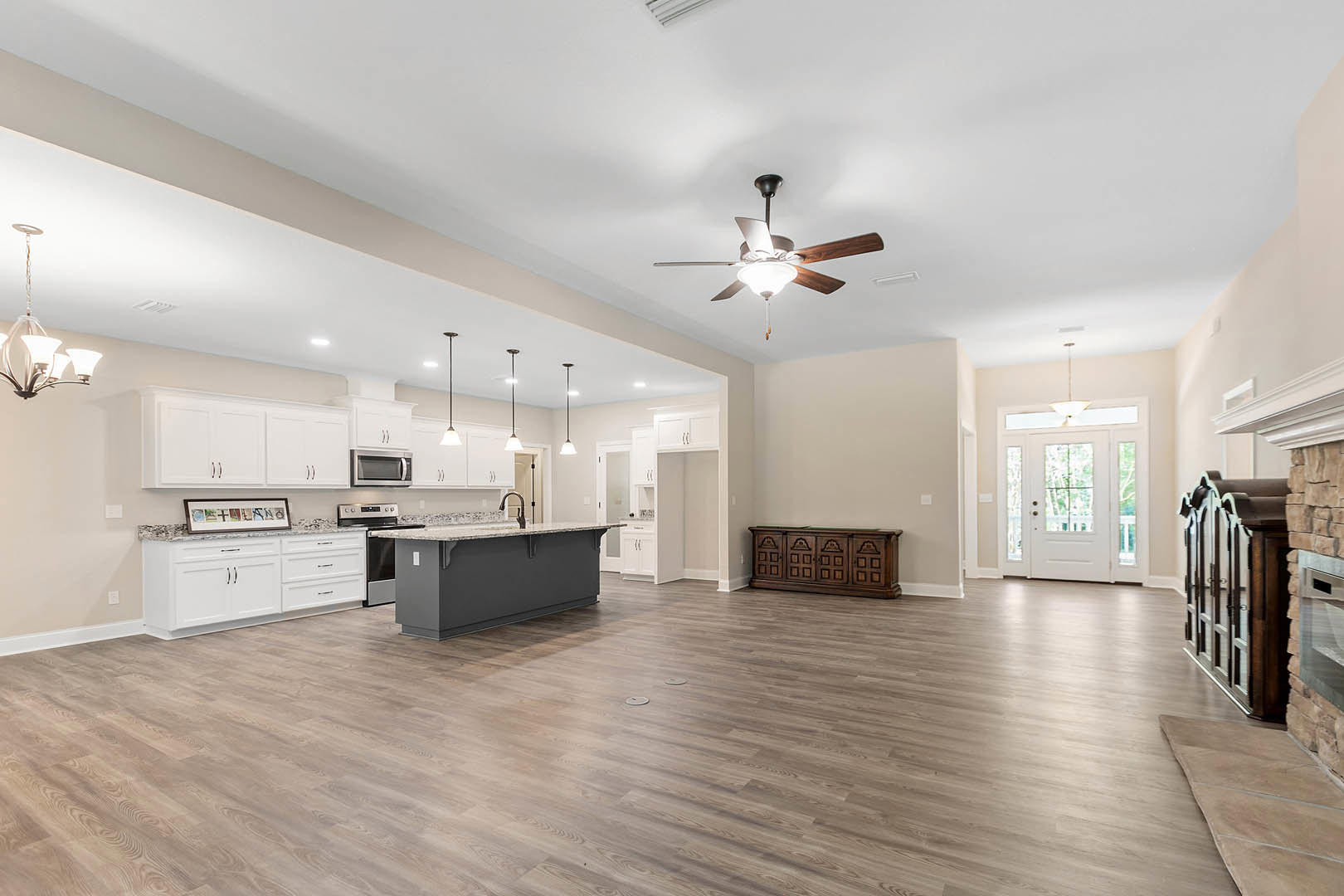 Spacious open floor plan featuring a kitchen island with marble countertop, wood flooring, wooden cabinetry against a white wall, open microwave oven, and a white door with glass