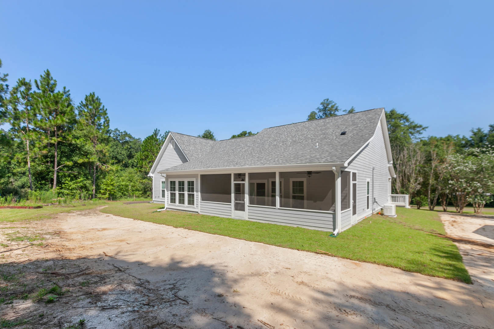 Two-story house with large covered porch, white window frames, gray roof, dirt driveway, grassy lawn, and blue sky overhead