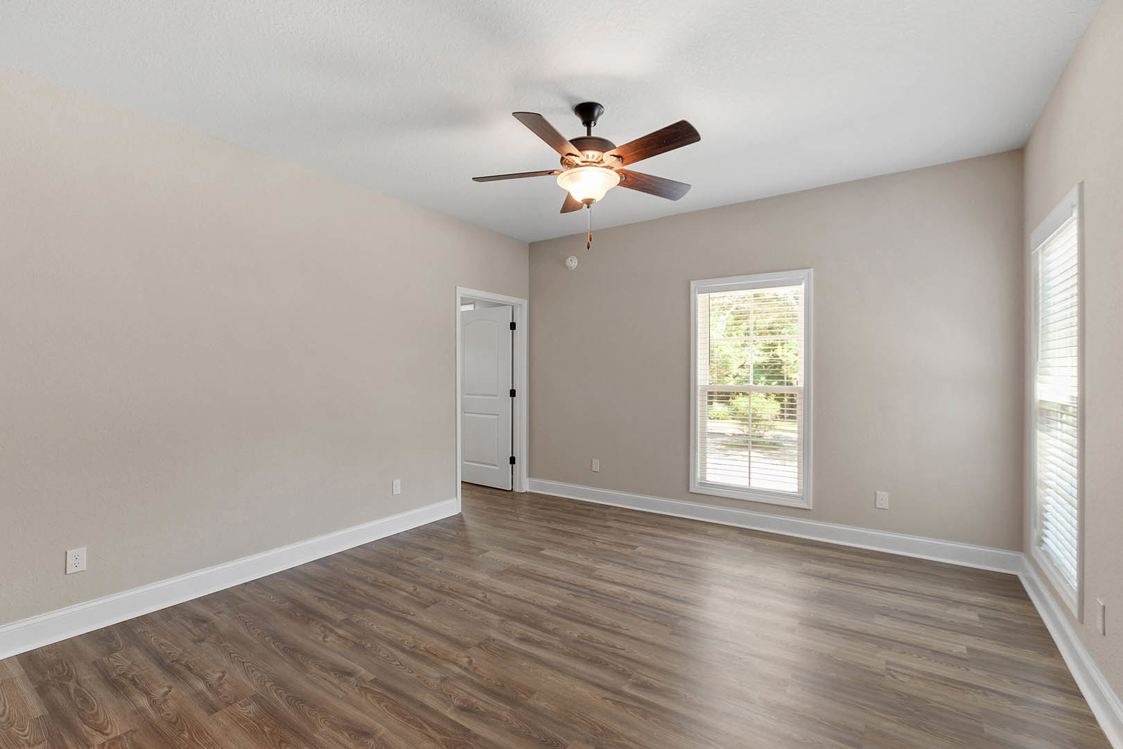 Ceiling fan with light fixture, wood flooring, white walls, window with blinds, white door with black lock, crown molding along plaster ceiling
