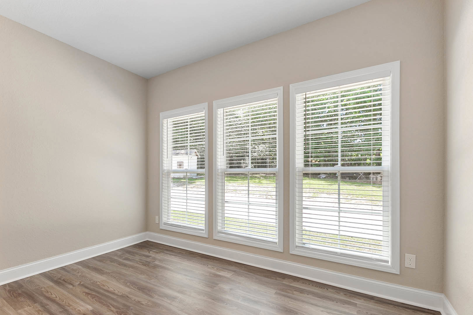 Wood flooring and white window blinds in a bright room with neutral walls