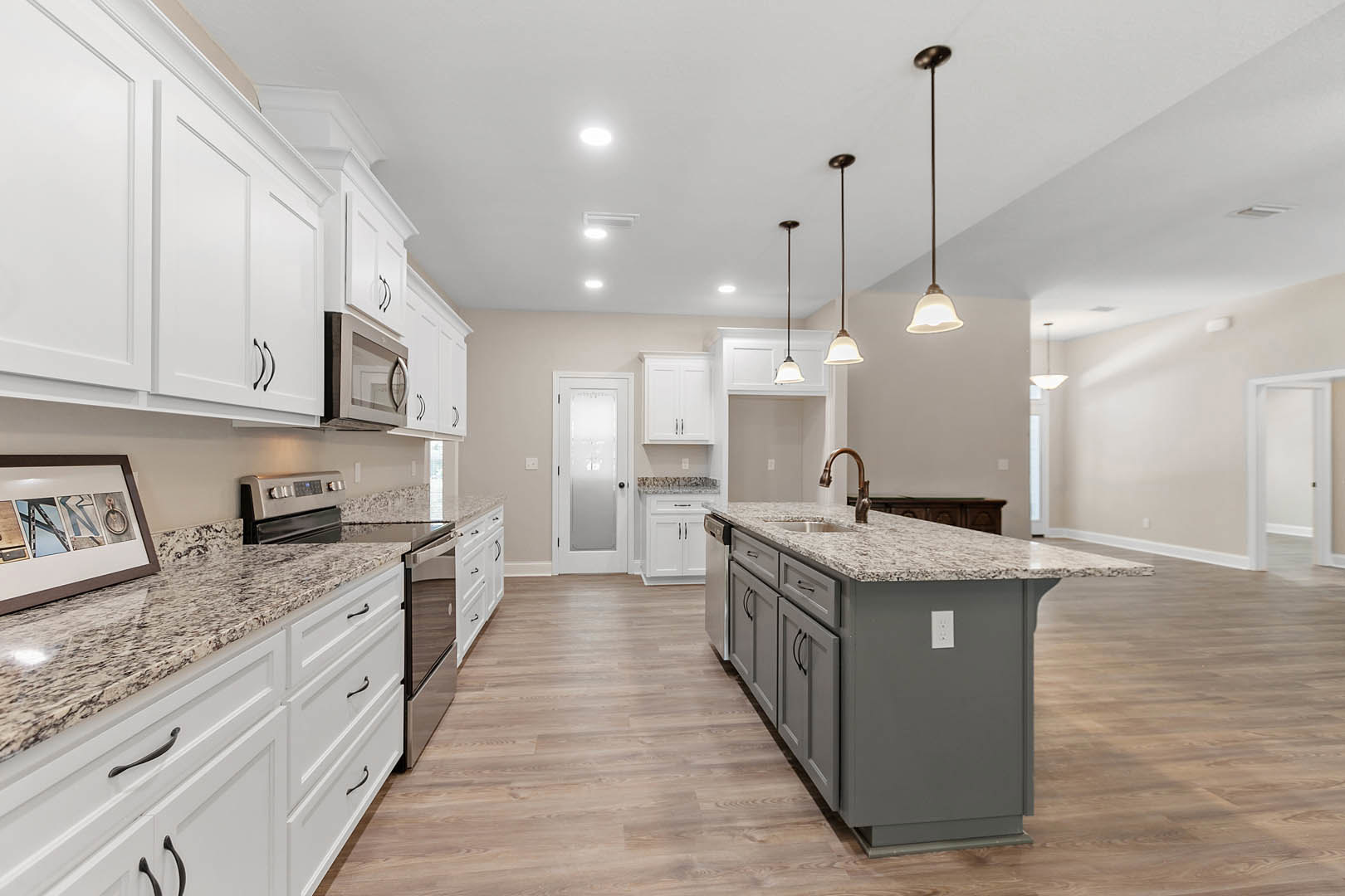 Granite countertops and white cabinets in a kitchen with tile flooring, kitchen island featuring a sink, stainless steel stove, white door with black handle, framed picture on