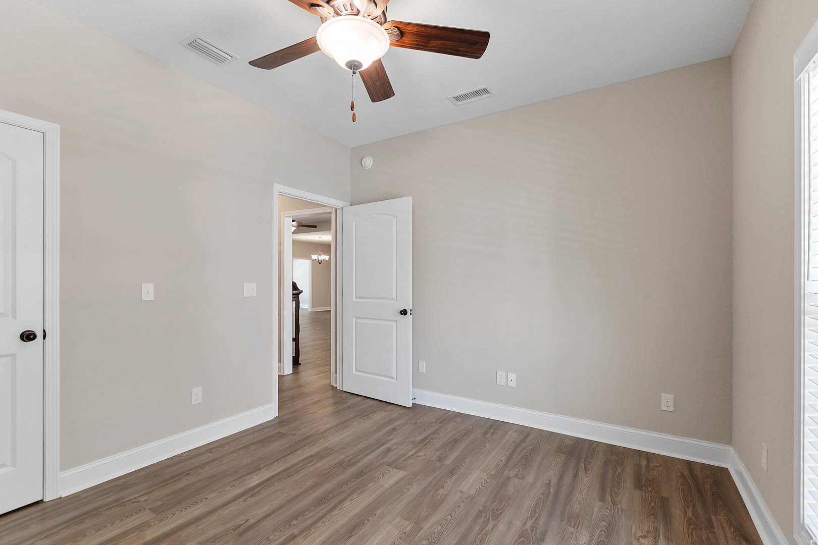 Ceiling fan with integrated light fixture above wood laminate flooring, white door with black knob partially open, neutral walls and trim.