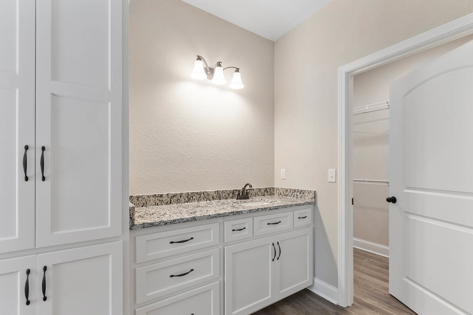 Bathroom with white cabinets featuring black handles, marble countertop with black and white veining, chrome faucet, white door, and modern light fixture.