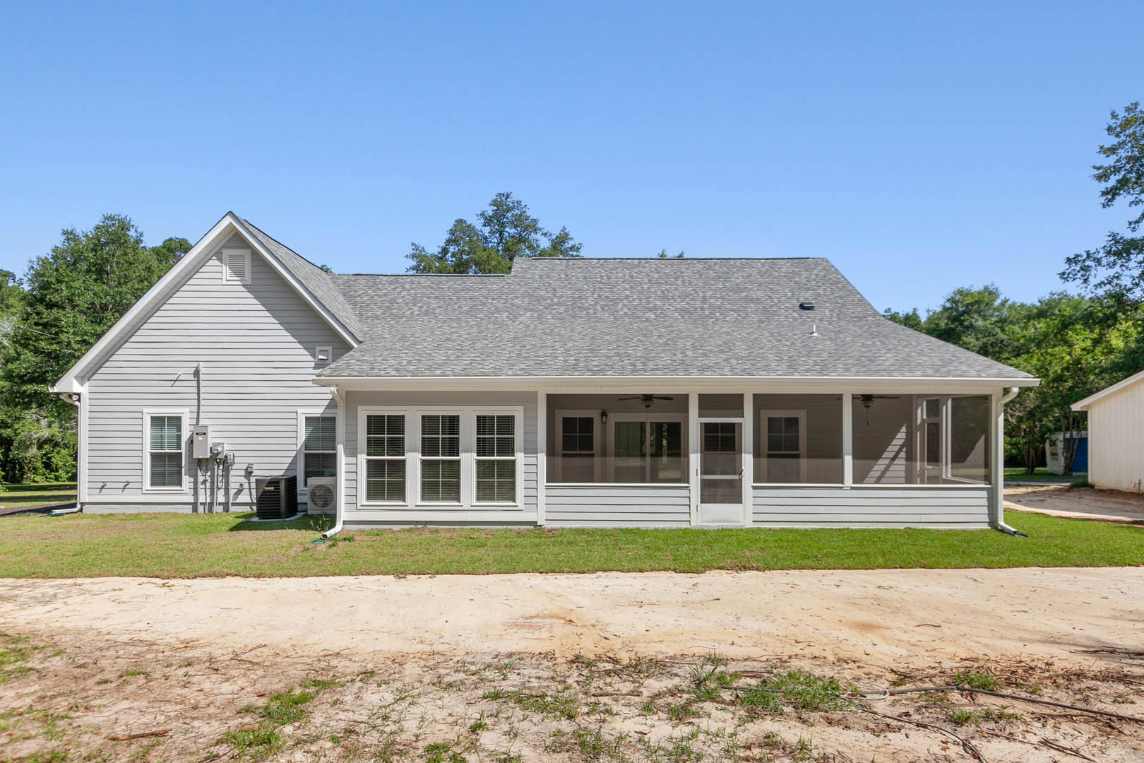 Two-story house with white siding, several grid windows, covered porch, dirt road leading to entrance, grassy yard, mature trees, and Robert Frost Farm visible in the background