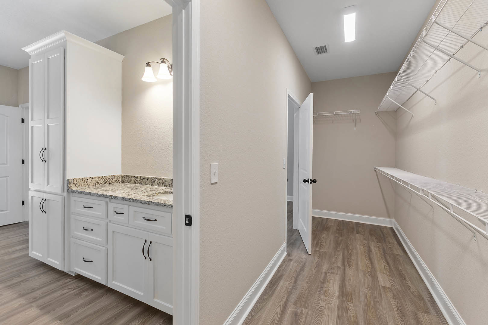 White cabinets with black handles, wood plank flooring, recessed ceiling light, wall-mounted shelf, white door with black hardware, neutral plaster walls.