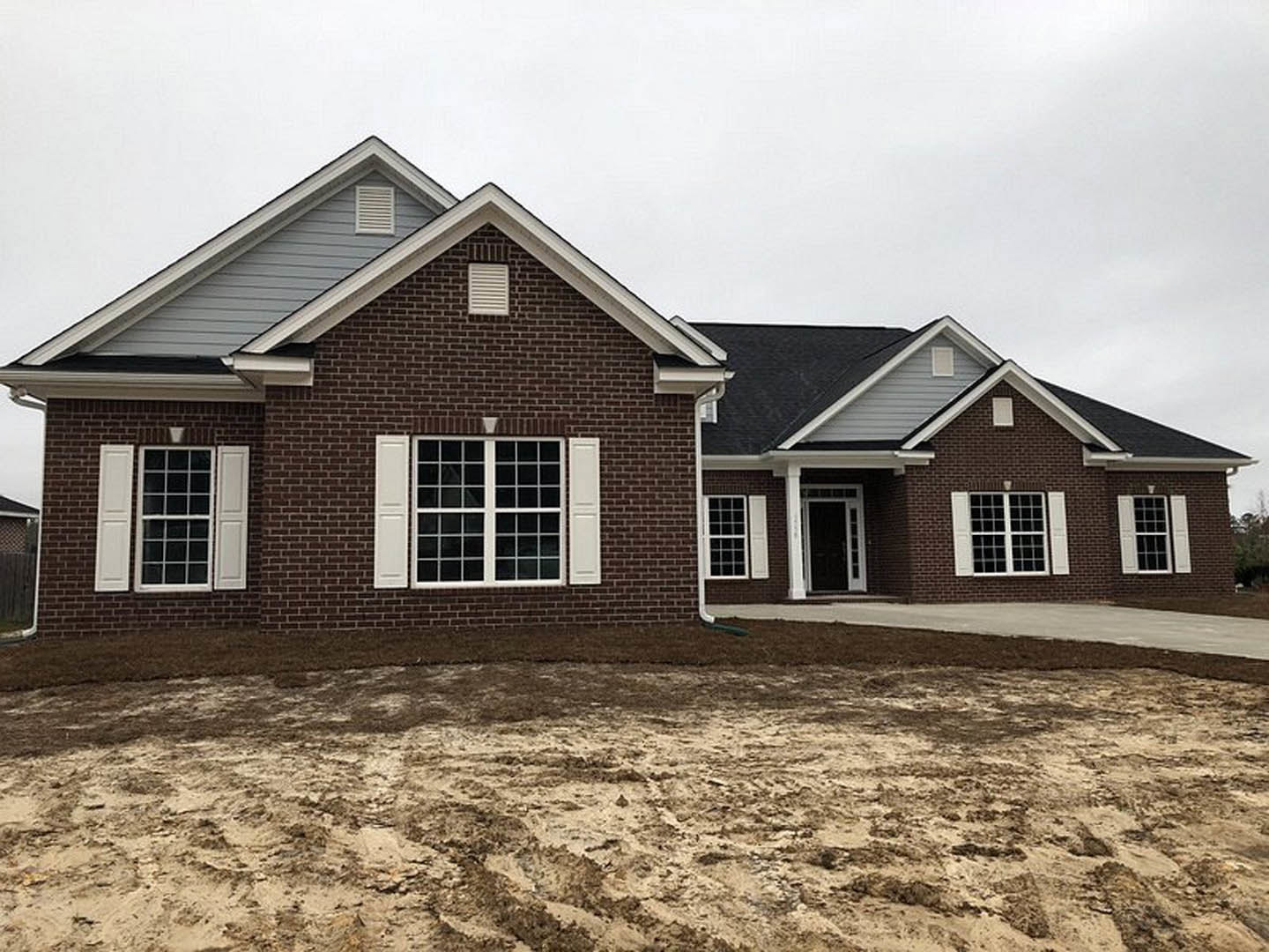 Brick exterior wall with white vent, multi-pane window, and dirt yard in front of custom home
