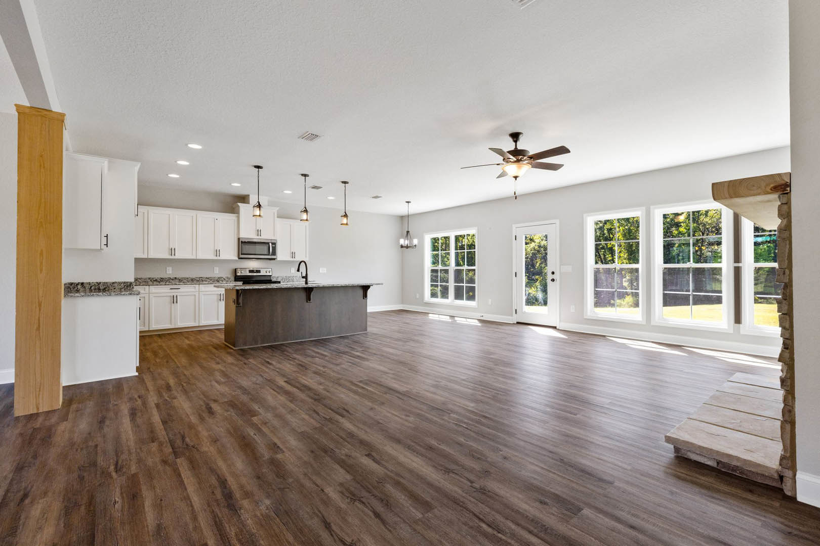 Spacious open floor plan featuring hardwood flooring, marble countertop kitchen, white cabinetry, built-in microwave, ceiling fan with light, and adjacent dining area