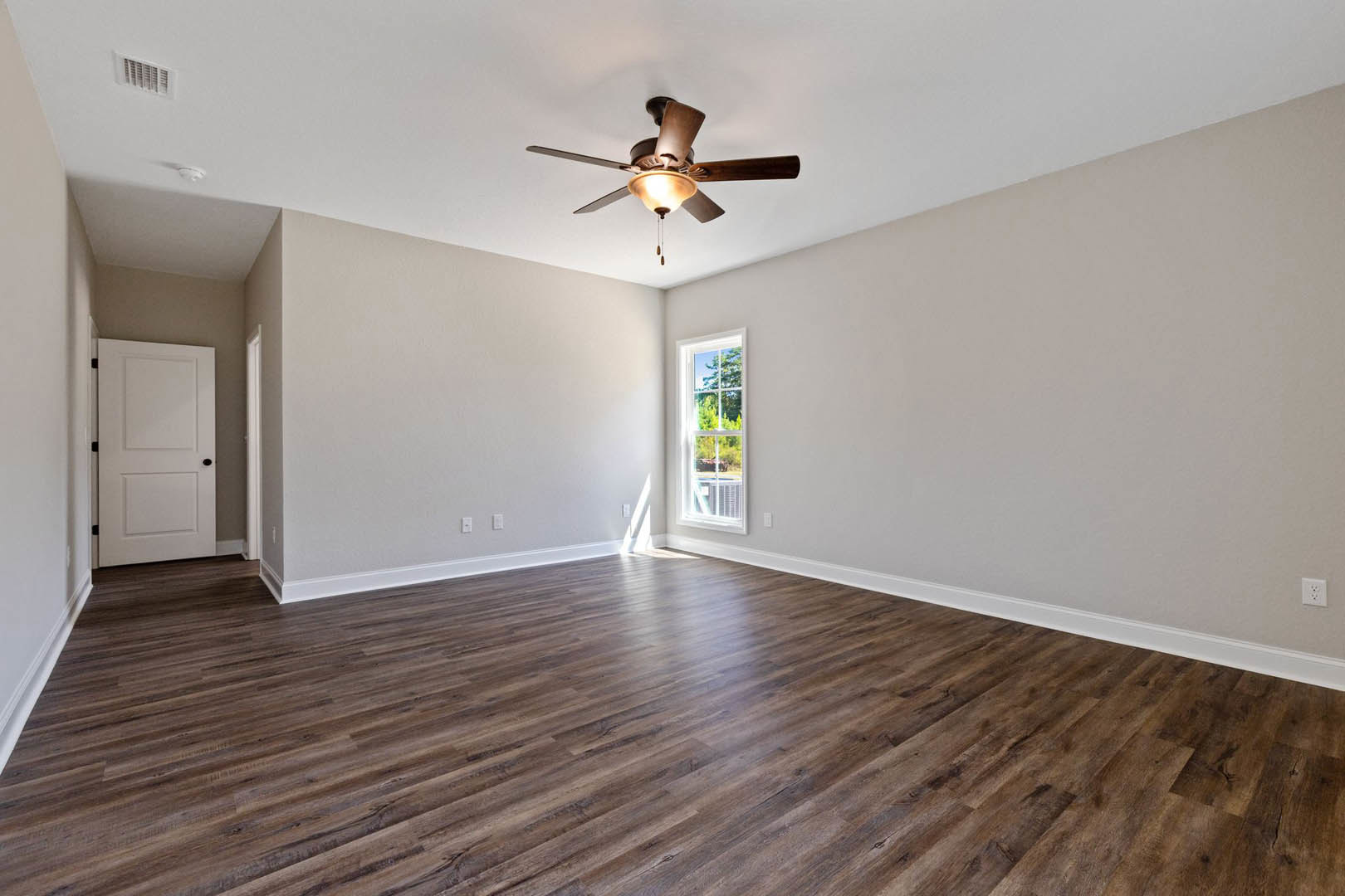 Ceiling fan with light fixture, wood flooring, white door with black knobs, window overlooking trees, wall vent, neutral plaster walls