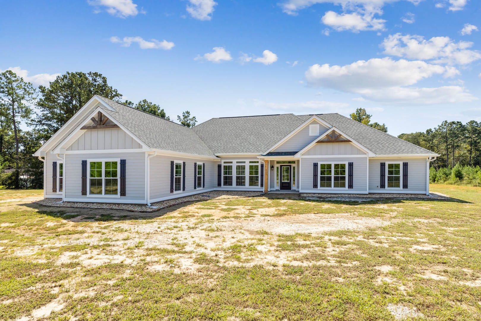 Two-story home with white siding, black front door, white-framed windows, covered porch, manicured grass yard, and blue sky with scattered clouds