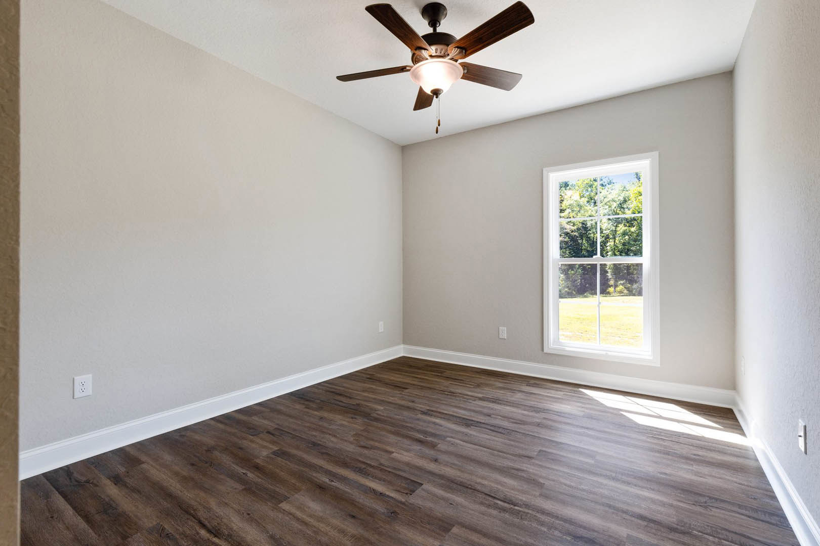Ceiling fan with light fixture mounted on white plaster ceiling, large window overlooking trees, hardwood floor, neutral walls