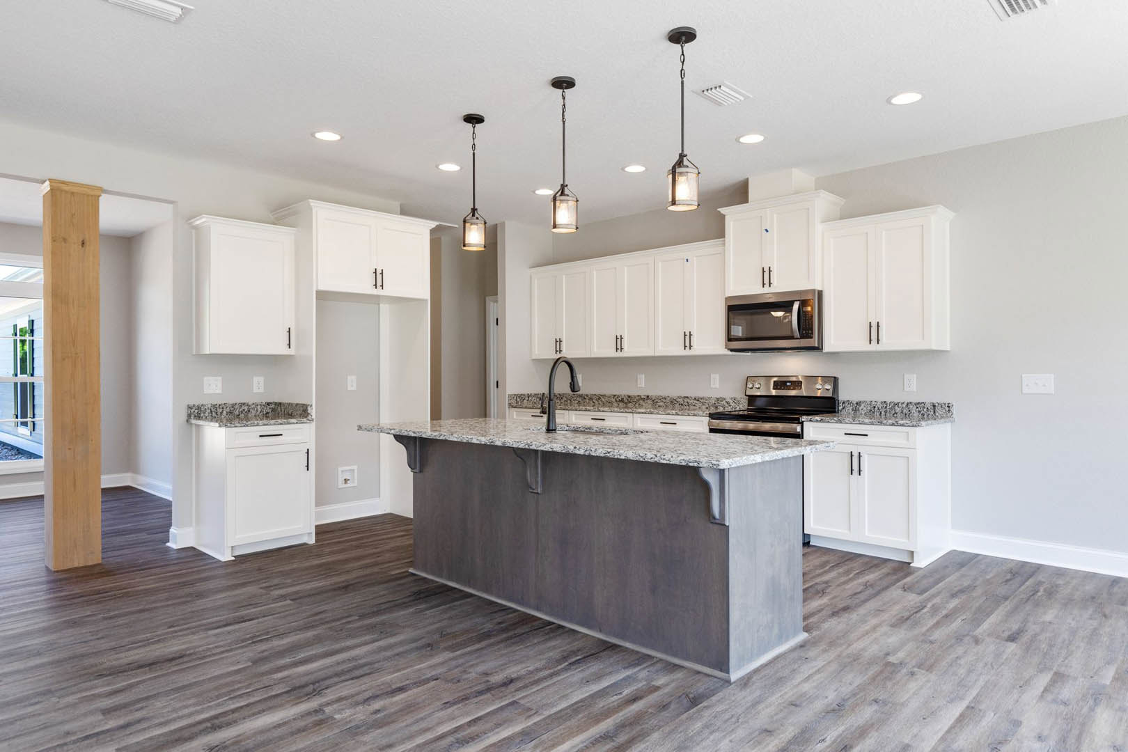 Spacious kitchen featuring a large marble island, stainless steel stove, wood cabinetry, built-in microwave, white door with black handle, and polished flooring.
