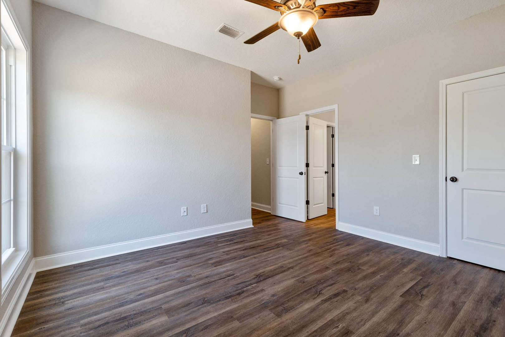 Ceiling fan with light fixture mounted above wood flooring, white door with black knobs, white rectangular window frame, neutral painted walls