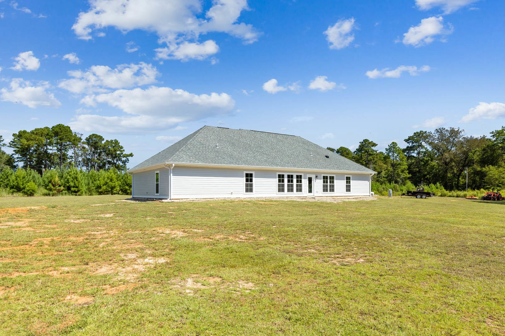 White farmhouse with gabled roof, surrounded by expansive green field under blue sky with scattered clouds