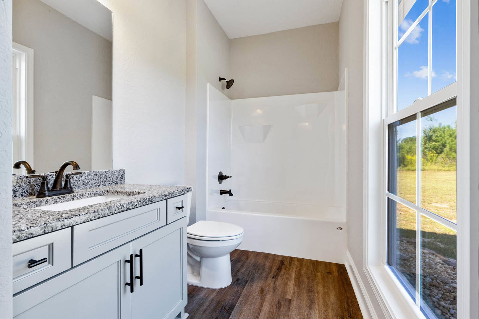 Modern bathroom featuring a white toilet, rectangular sink with chrome faucet, light tile flooring, white countertop, and a window overlooking a grassy field