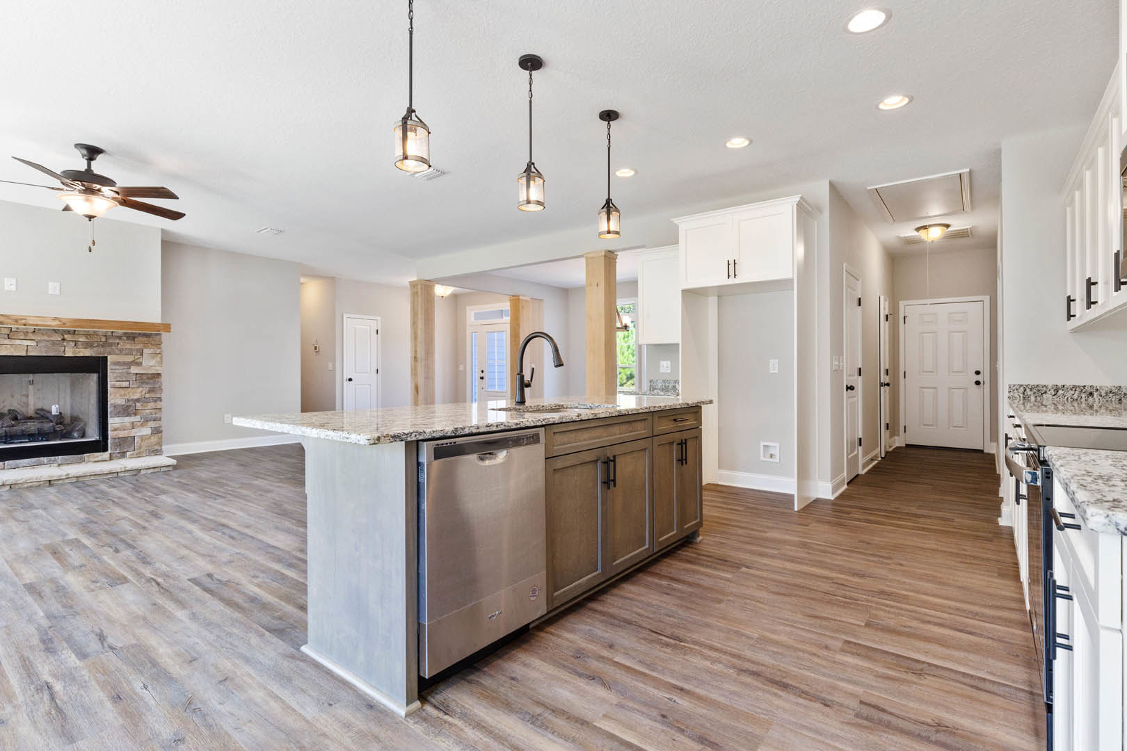 Spacious kitchen featuring a large central island with stone countertop, white cabinetry, stainless steel refrigerator, fireplace with stacked wood, white door with black hardware