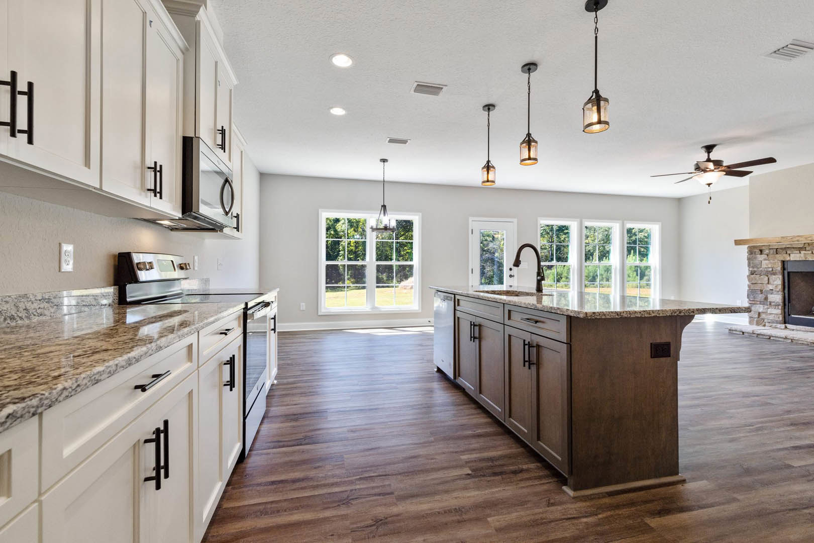 Kitchen with wood flooring, white shaker cabinets, quartz countertops, stainless steel stove, glass pendant light fixture, window above sink, brown accent wall with black trim