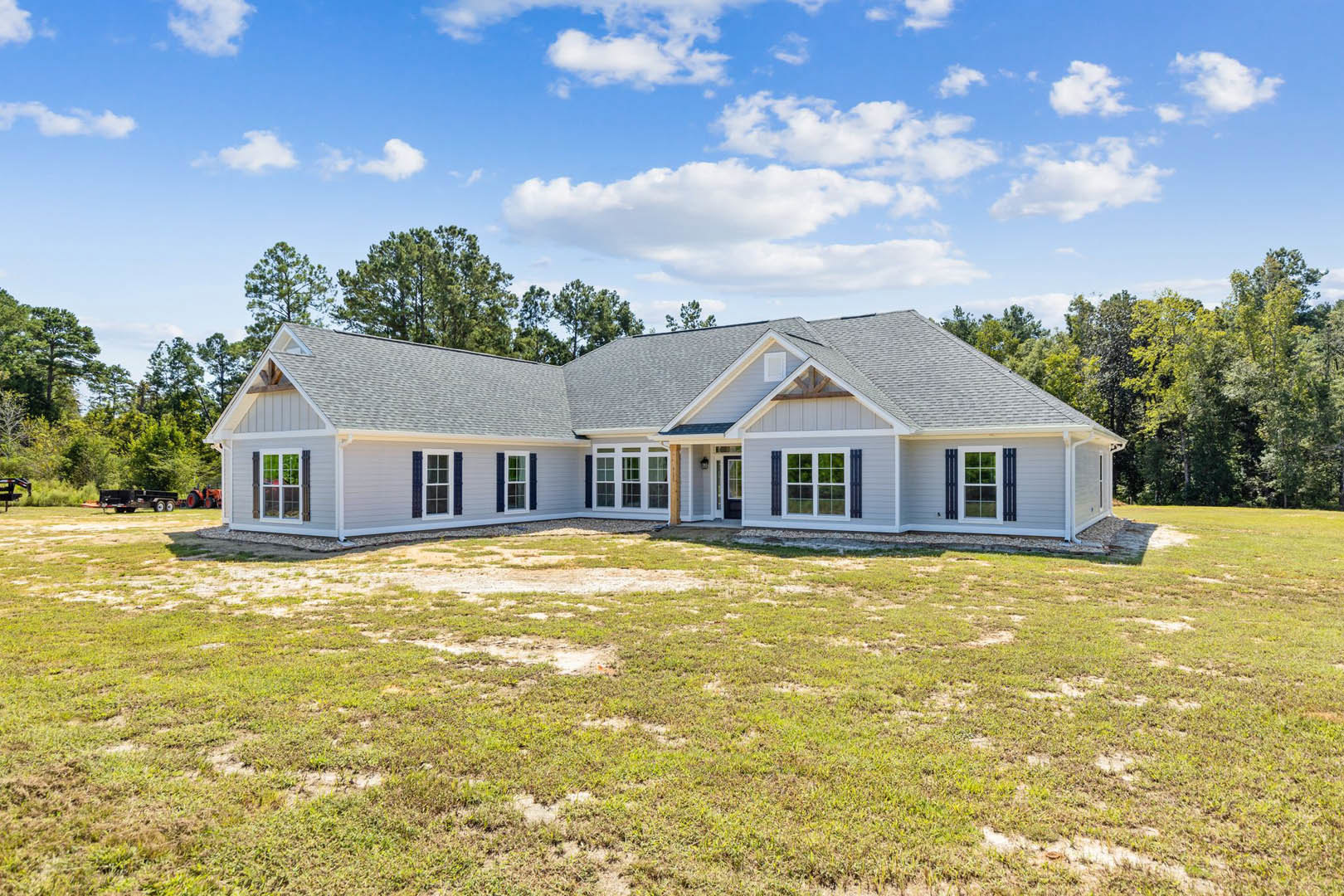 White custom home with blue roof, large windows, manicured lawn, mature trees in background, and partly cloudy sky overhead