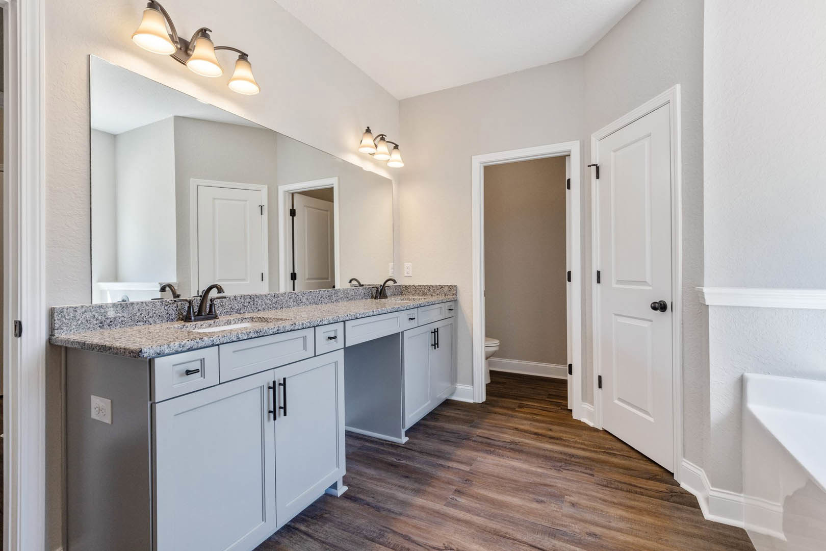 Bathroom with white cabinets, marble countertops, three-light fixture, white door with black handles, and tile flooring
