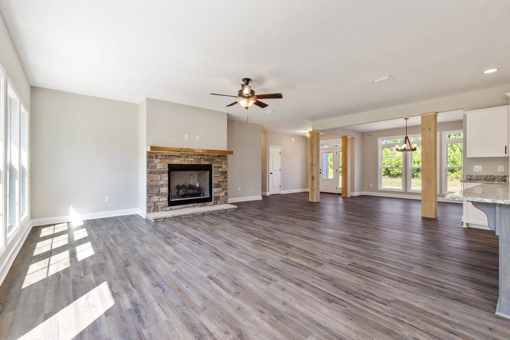 Spacious living room featuring brick fireplace with glass door, hardwood flooring, ceiling fan with light, and chandelier