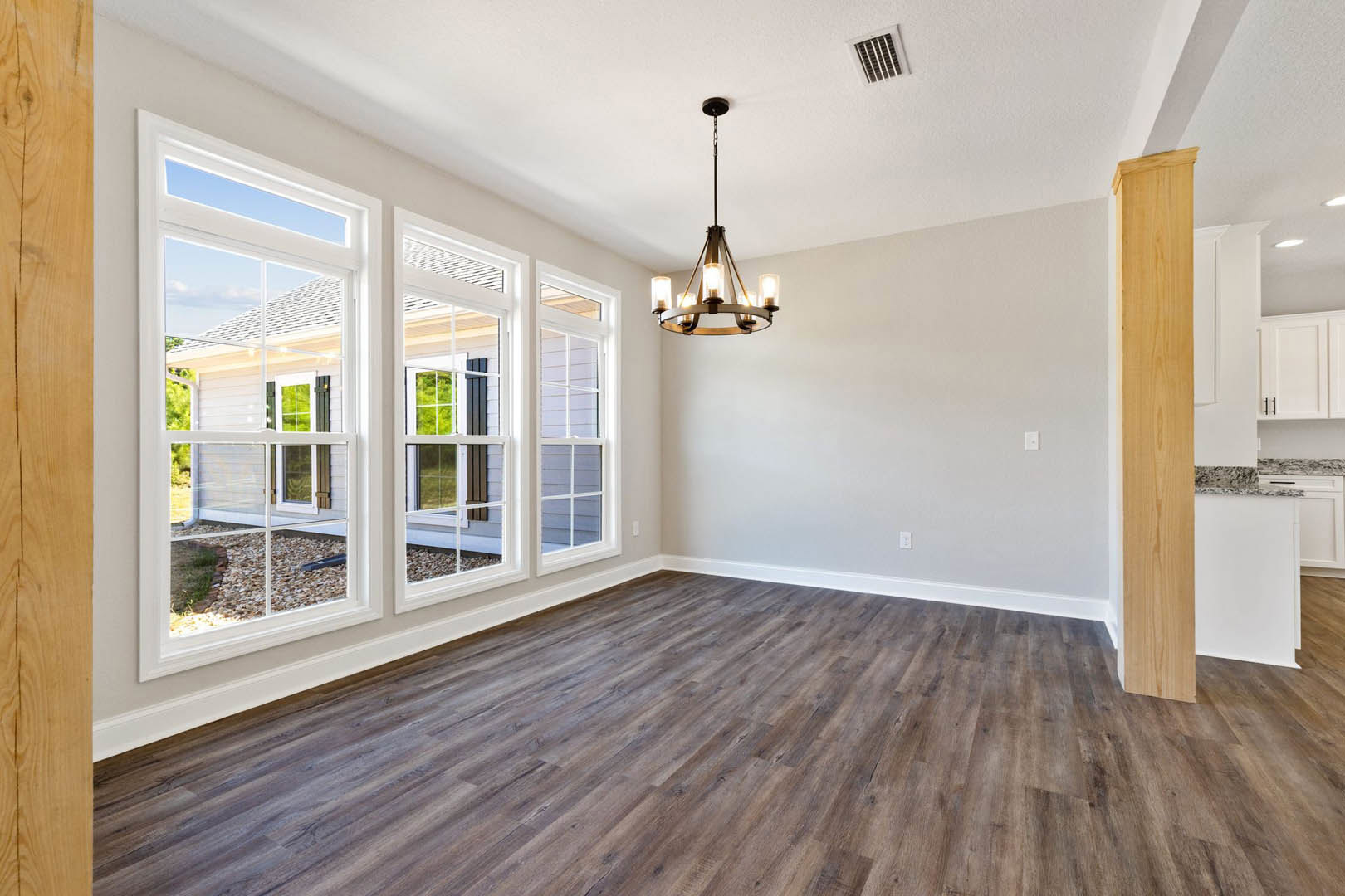 Chandelier hanging from white ceiling with recessed vent, row of tall windows along wall, hardwood flooring, wood panel accents