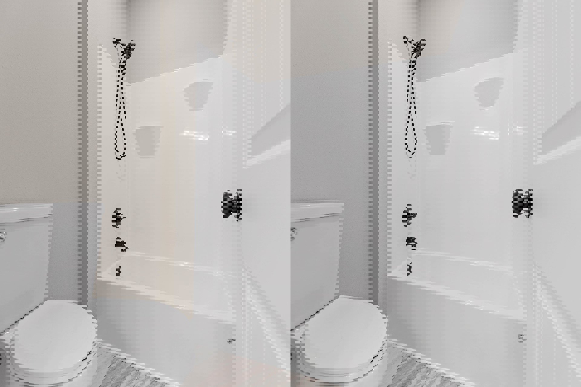 White bathtub with chrome shower head and hose, adjacent to a closed white toilet, set against white tiled walls in a modern bathroom.