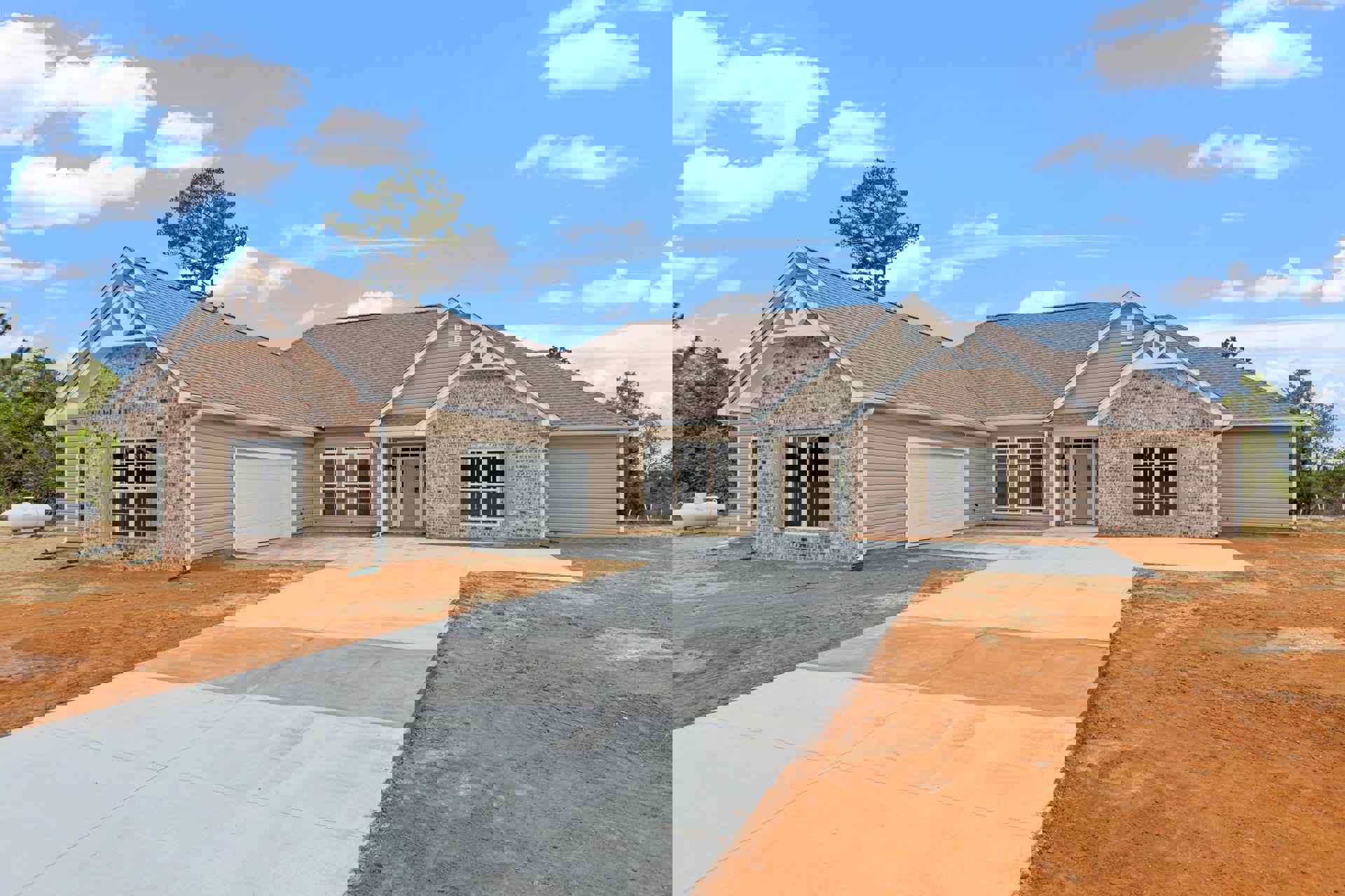 Modern two-story home with gray siding, prominent garage door, paved driveway, large windows, green-leafed trees, and cloudy sky overhead