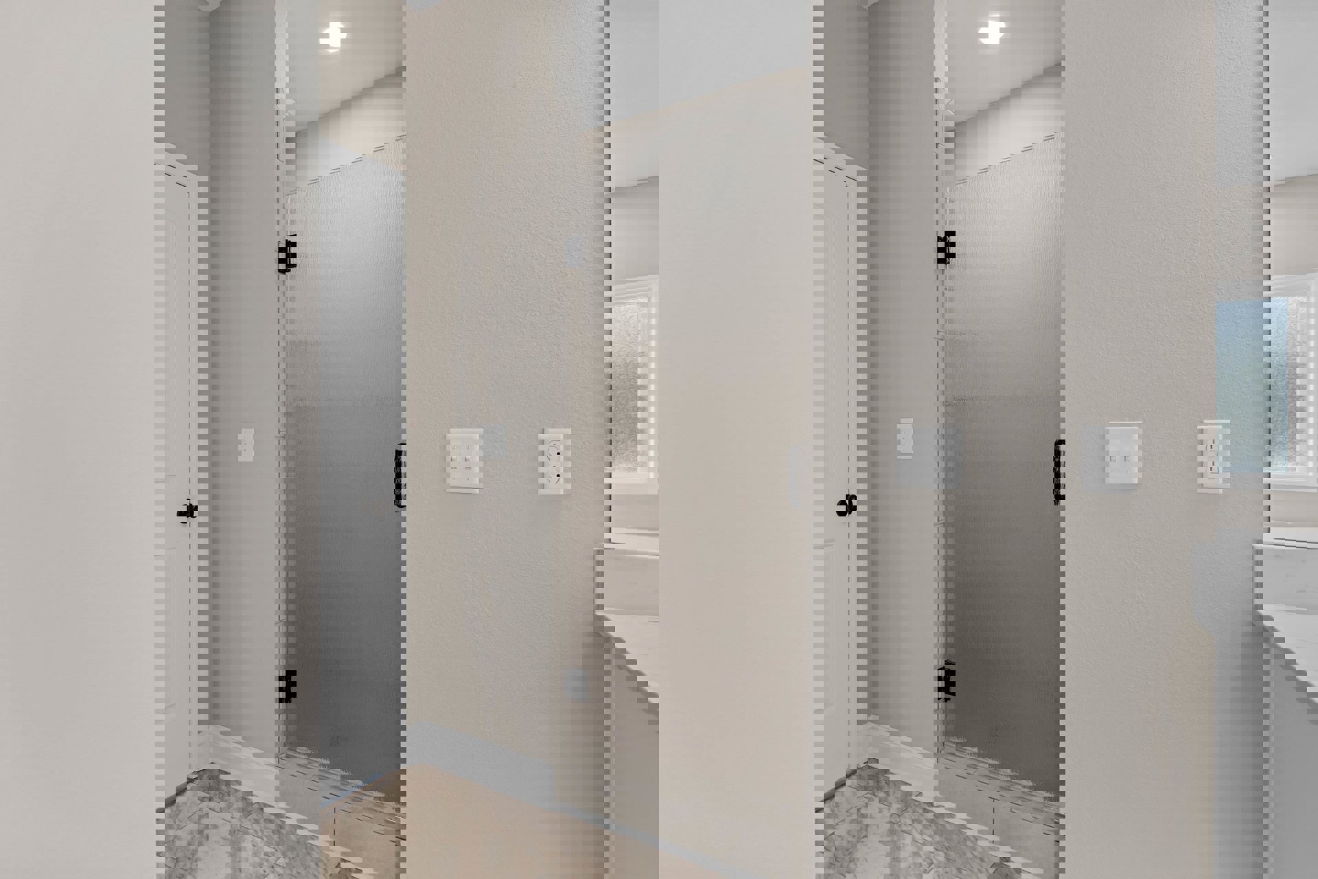 Walk-in shower with large white tile walls, chrome plumbing fixtures, frosted glass window, white countertop, recessed ceiling light, and modern light switch on plaster wall.