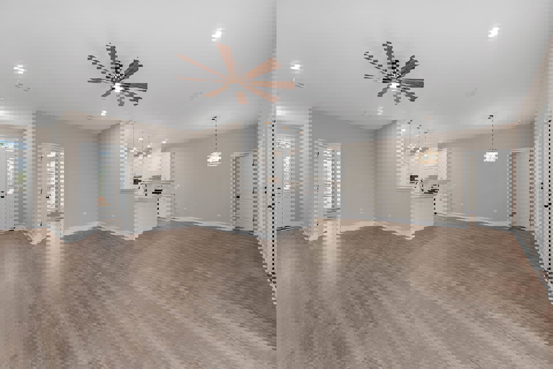 Spacious open floor plan featuring wood laminate flooring, ceiling fan with light, adjacent kitchen area, white doors with black hardware, and a modern chandelier.