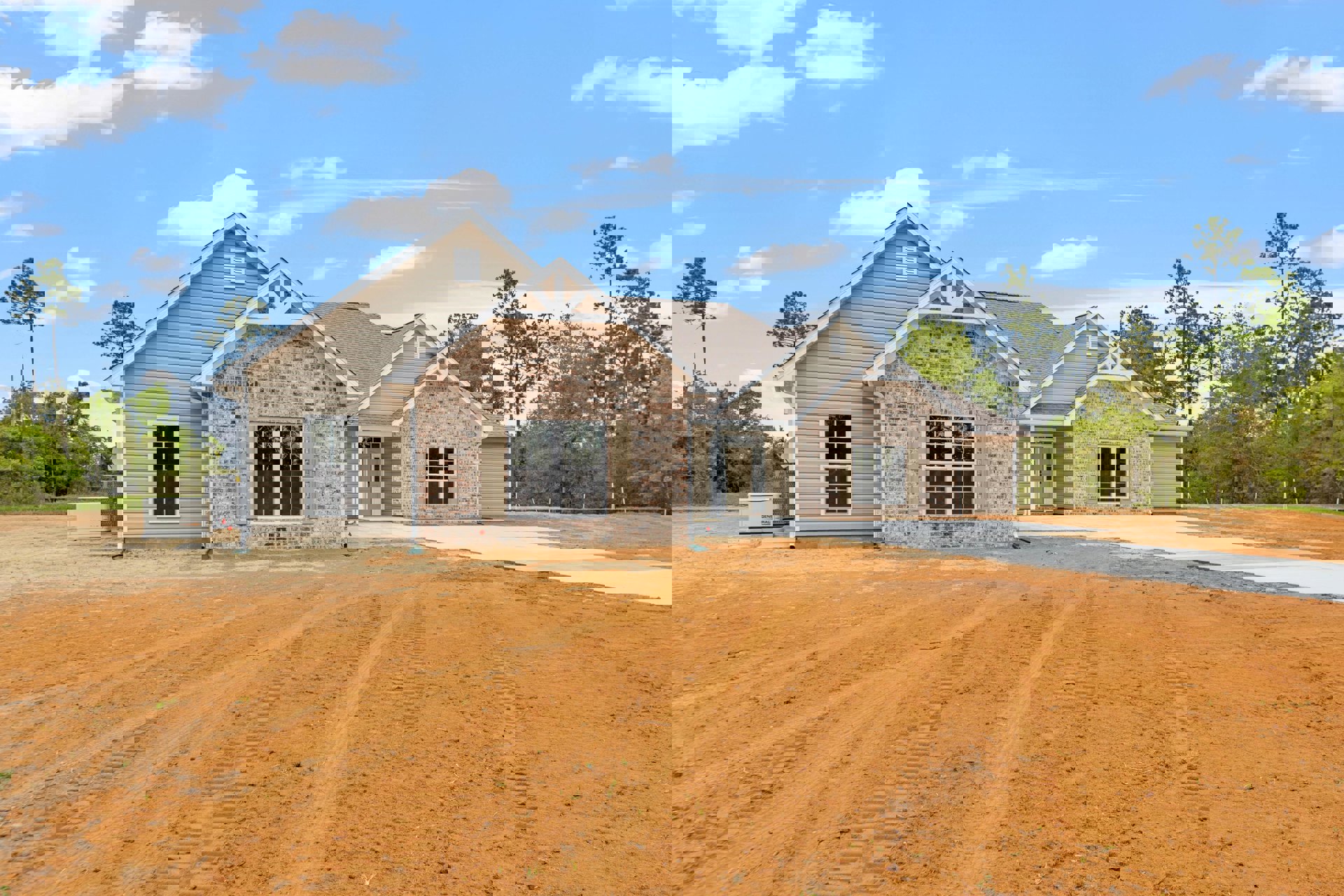 Brick house with white-framed window, tire tracks on dirt road in front, trees and cloudy sky in background