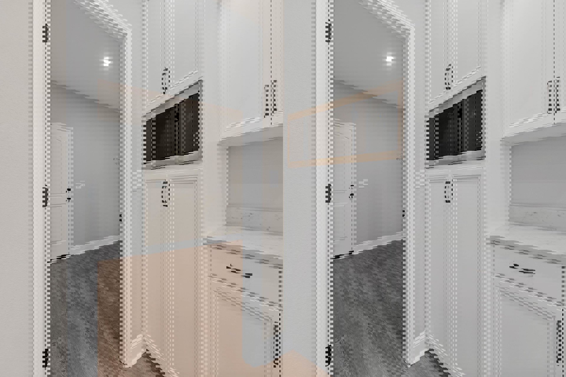 White kitchen cabinets with silver handles, wood flooring, built-in microwave, white door with matching frame, and light-colored countertops.