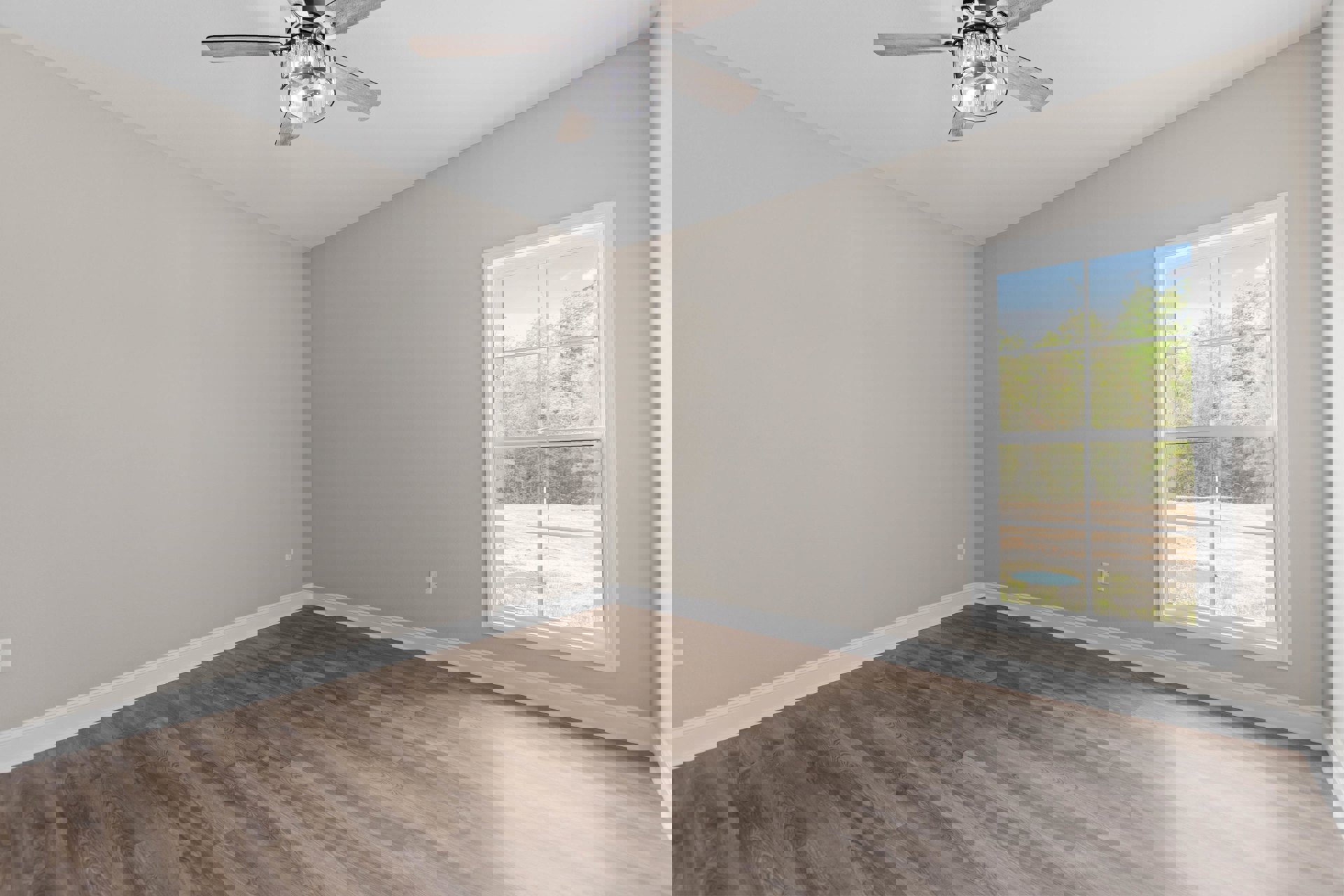 Wood floor room with white trim, ceiling fan and light fixture, large window showing trees and blue sky with clouds