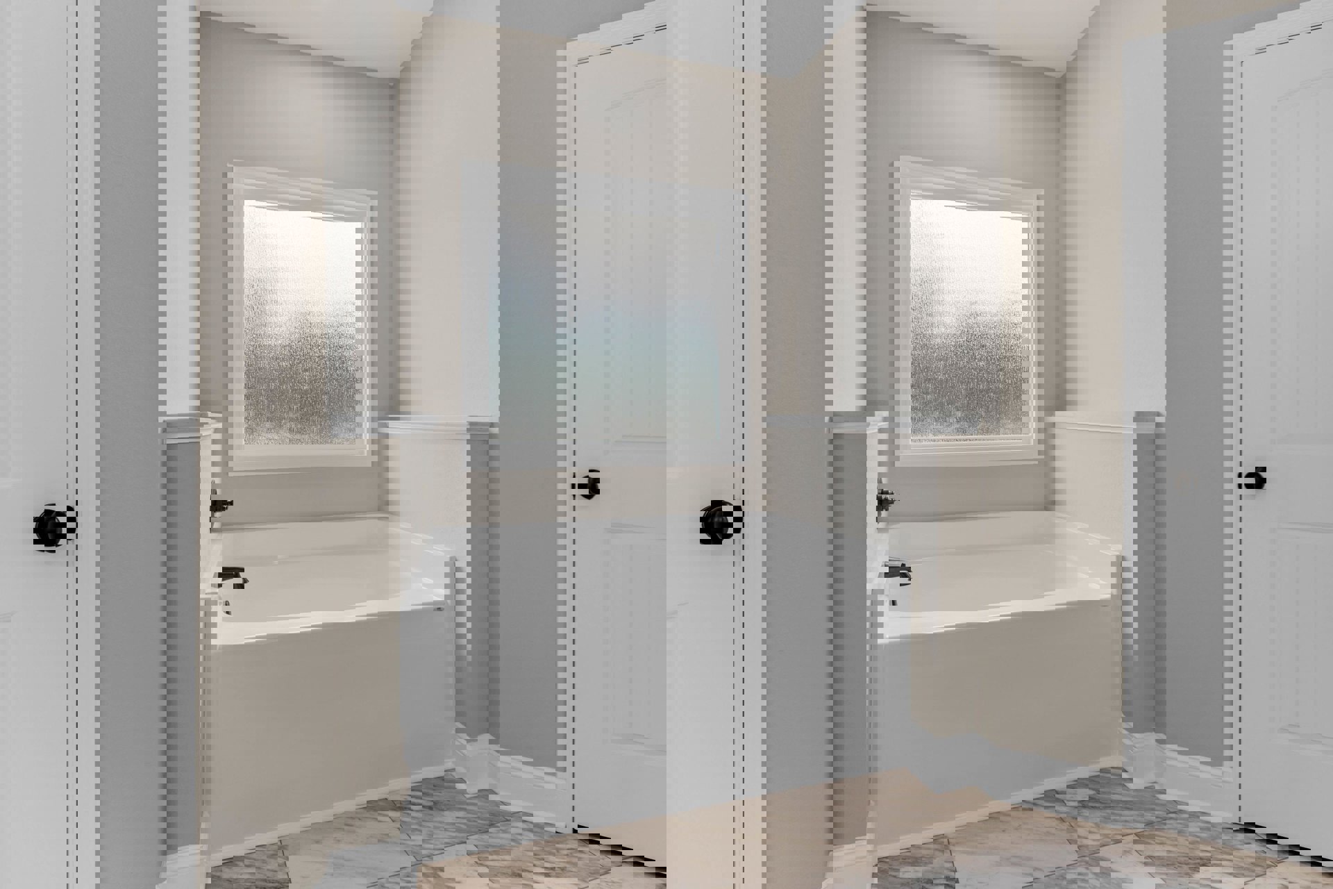 Freestanding white bathtub with matte black faucet, marble tile floor, frosted glass window, and white door with round black handle in modern bathroom