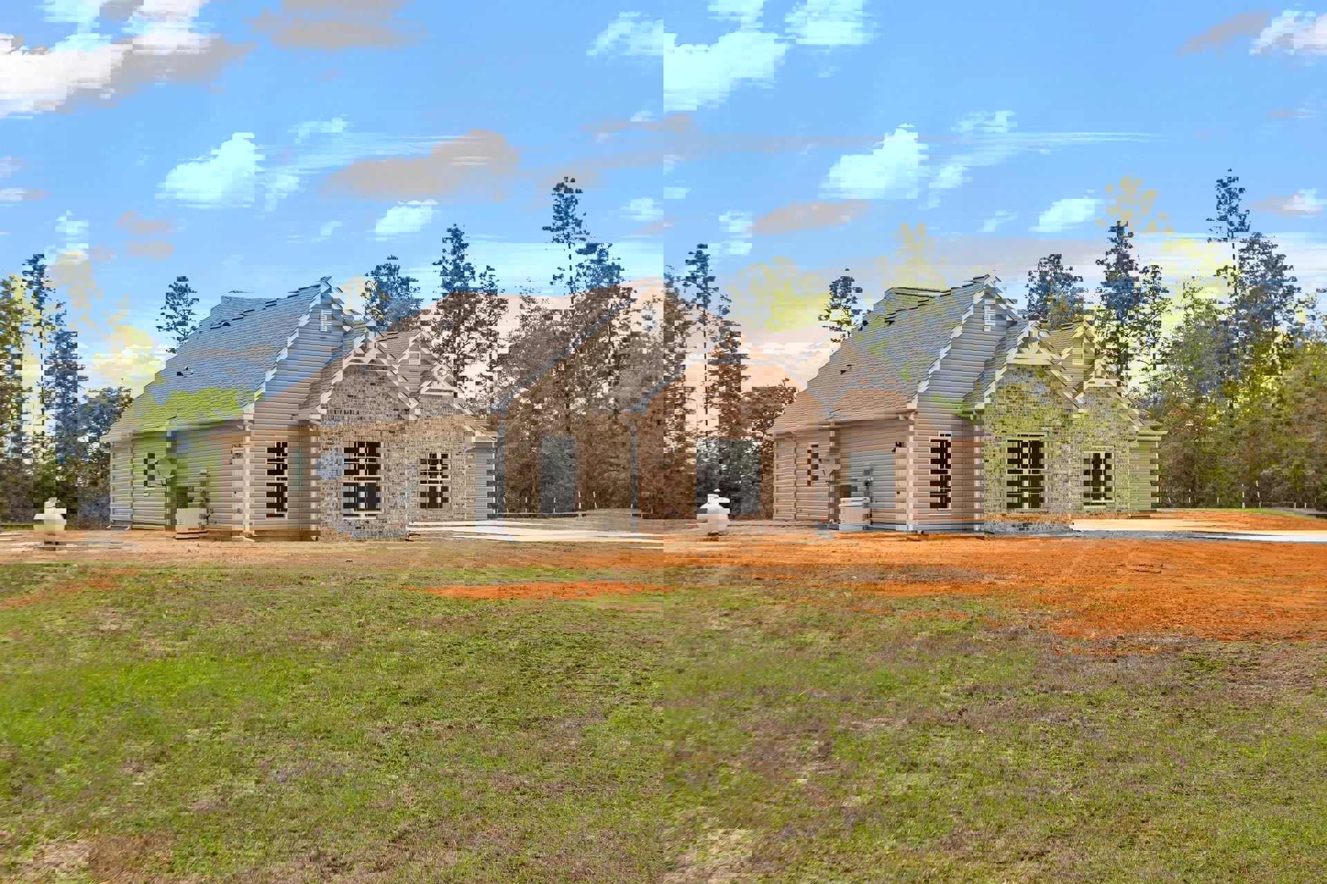 Brick house with gabled roof, white-framed windows, large grassy yard, mature trees, white water tank on dirt area, cloudy sky overhead