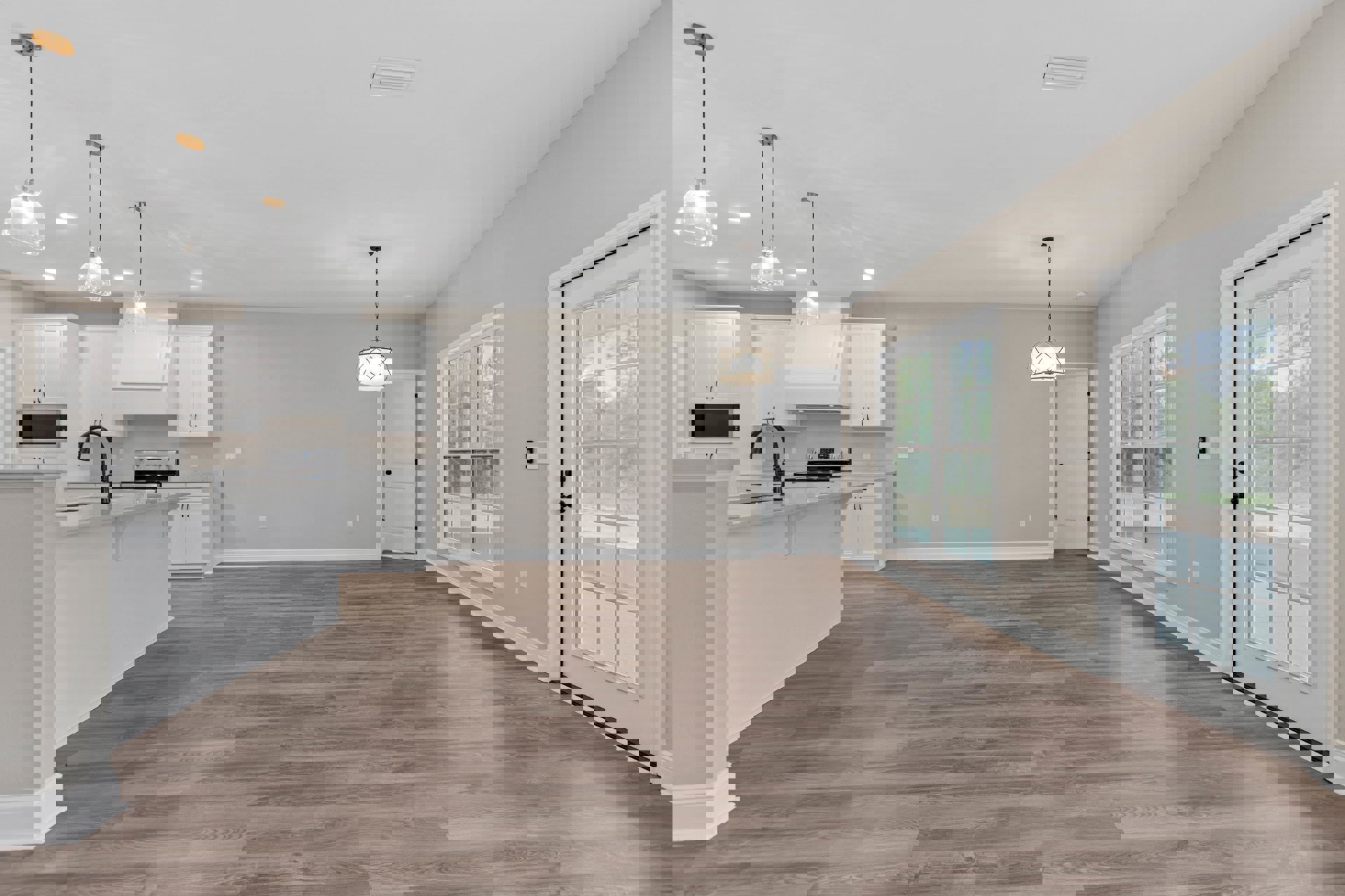 Open kitchen with hardwood flooring, white cabinetry, stainless steel appliances, white door with glass panes and black knobs, chain hanging from ceiling, adjacent living area with